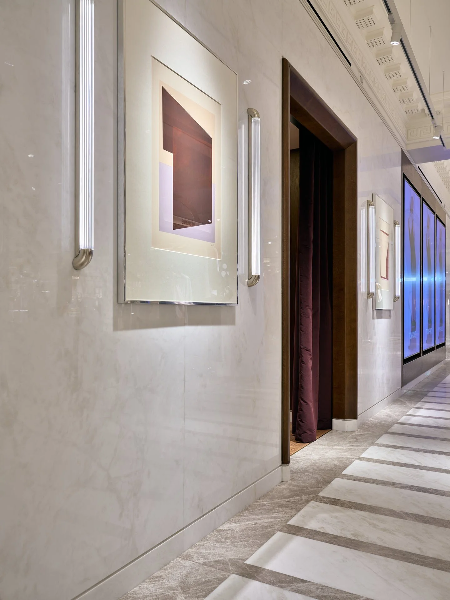 Polished pale marble wall cladding with framed artwork and lighting beside a patterned marble floor by stoneCIRCLE - photo Marco Joe Fazio STUDIO