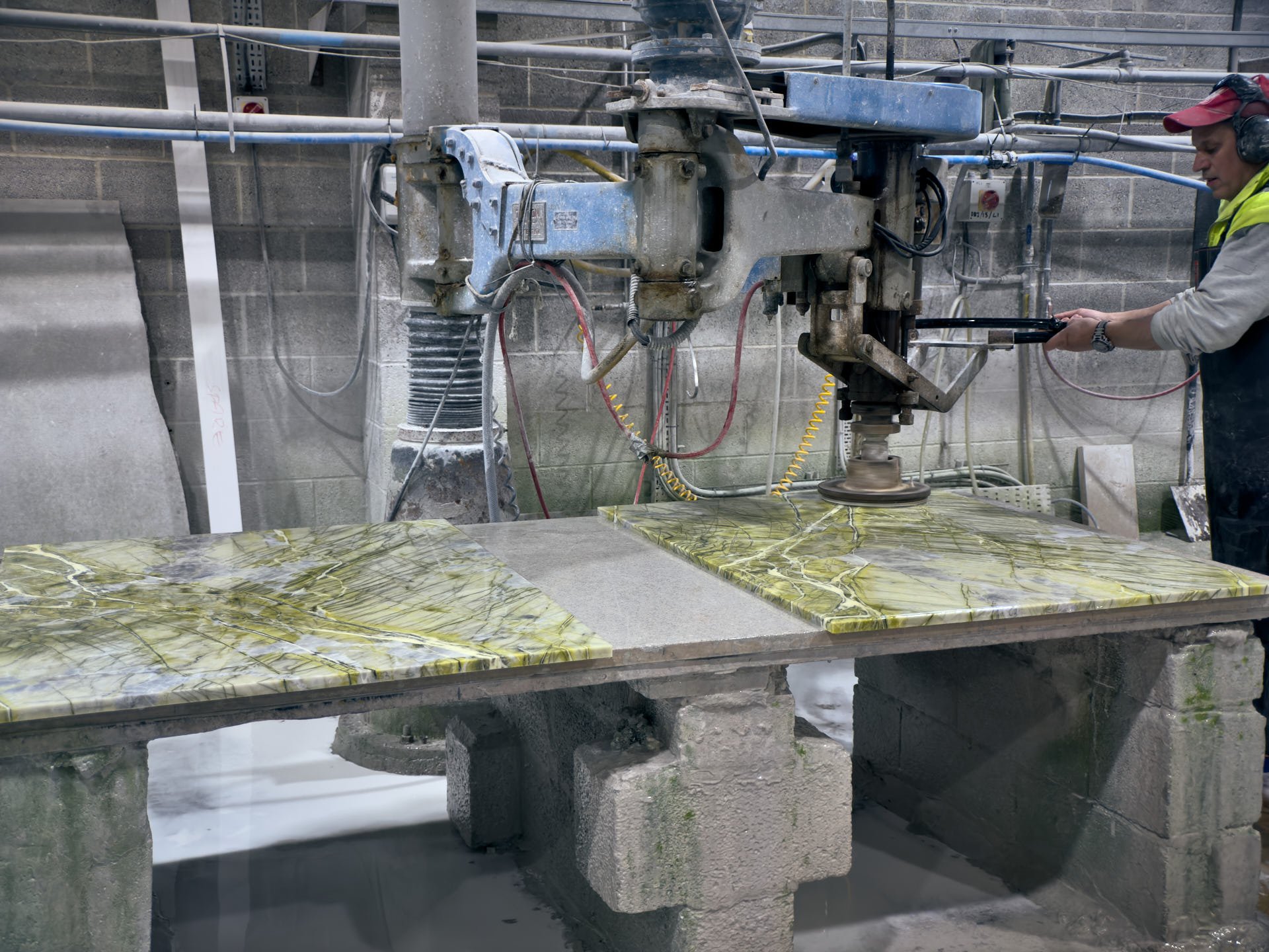 A mason operates the Jenny Lind radial-arm polisher over green stone pieces on a workshop bench.
