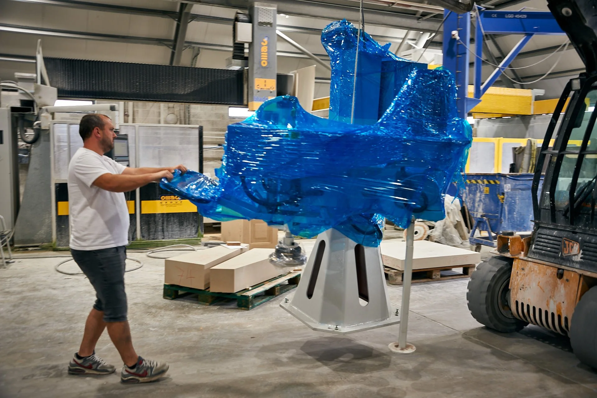 A worker guides the blue-wrapped replacement polisher as a telehandler moves it inside the stoneCIRCLE factory.