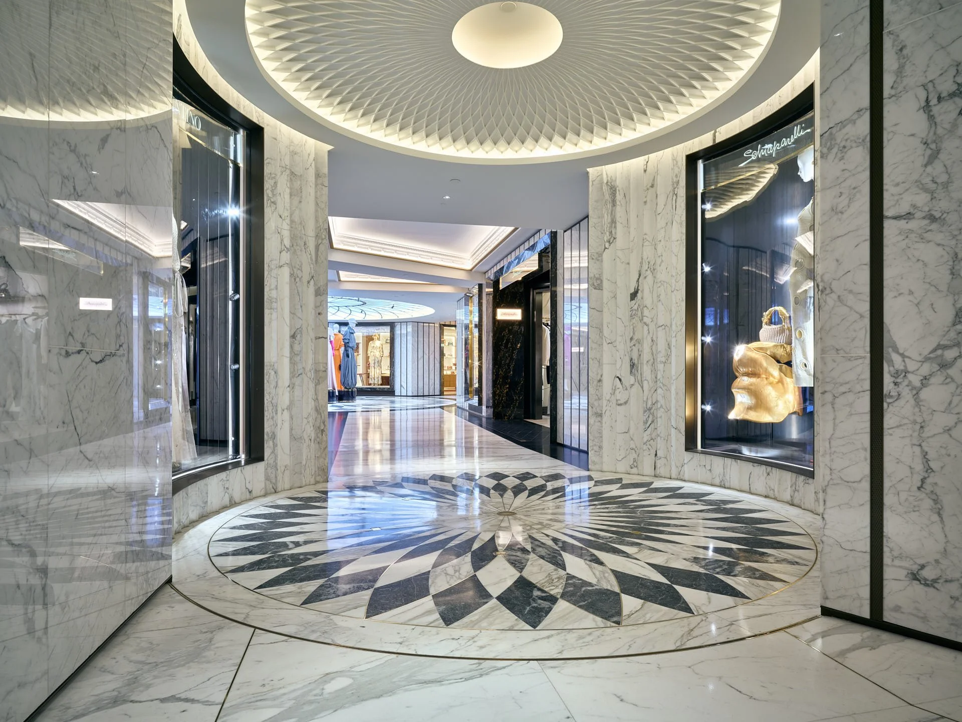 Wide Harrods hallway with a circular radial stone floor, marble-clad walls, illuminated displays and a second patterned area beyond. Fabrication and installation by stoneCIRCLE - photo Marco Joe Fazio Studio.