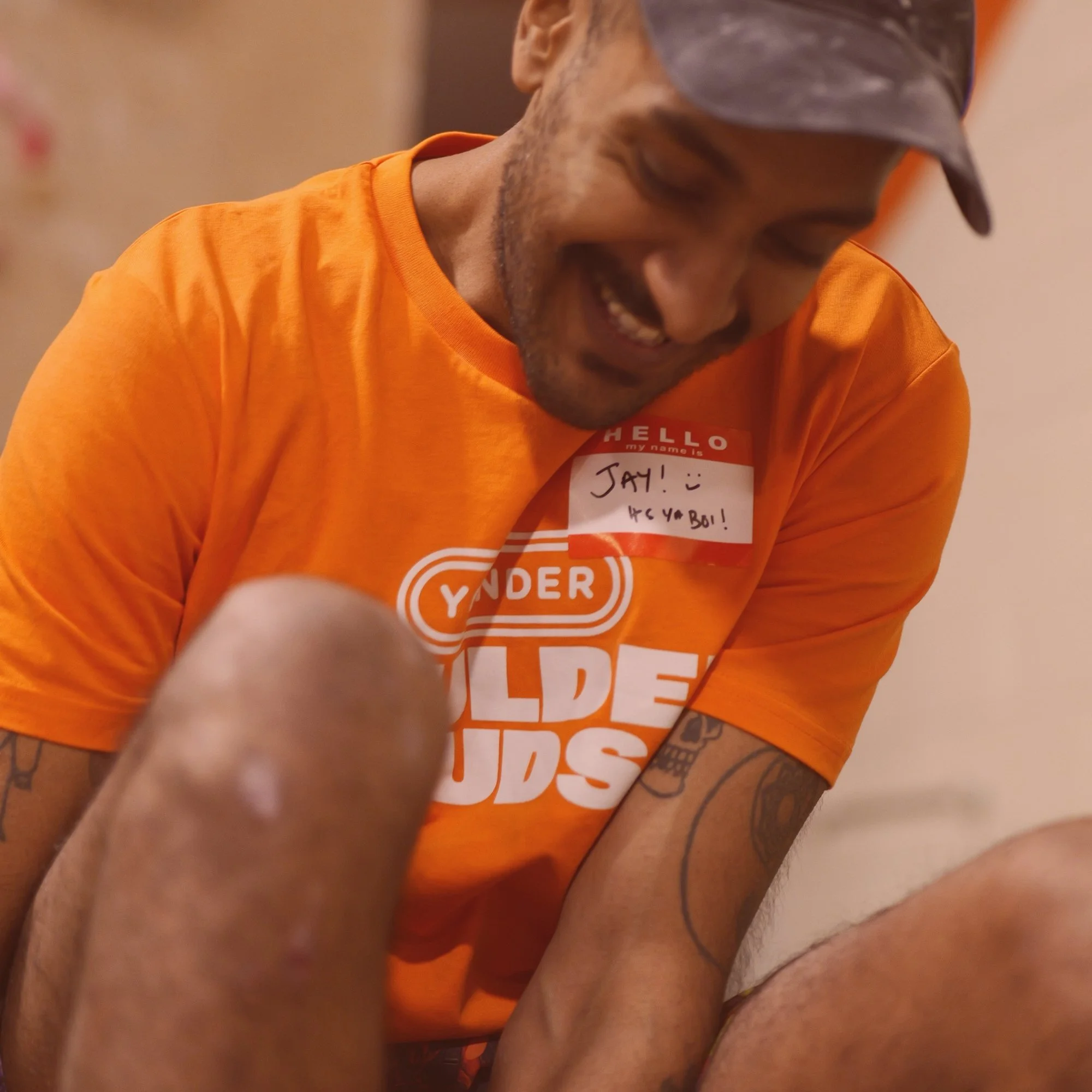 A man smiling while wearing an orange T-shirt that has the text 'Yonder' and 'Older Kids' on it, with a name tag that says 'Jay! :) You & Bo!'