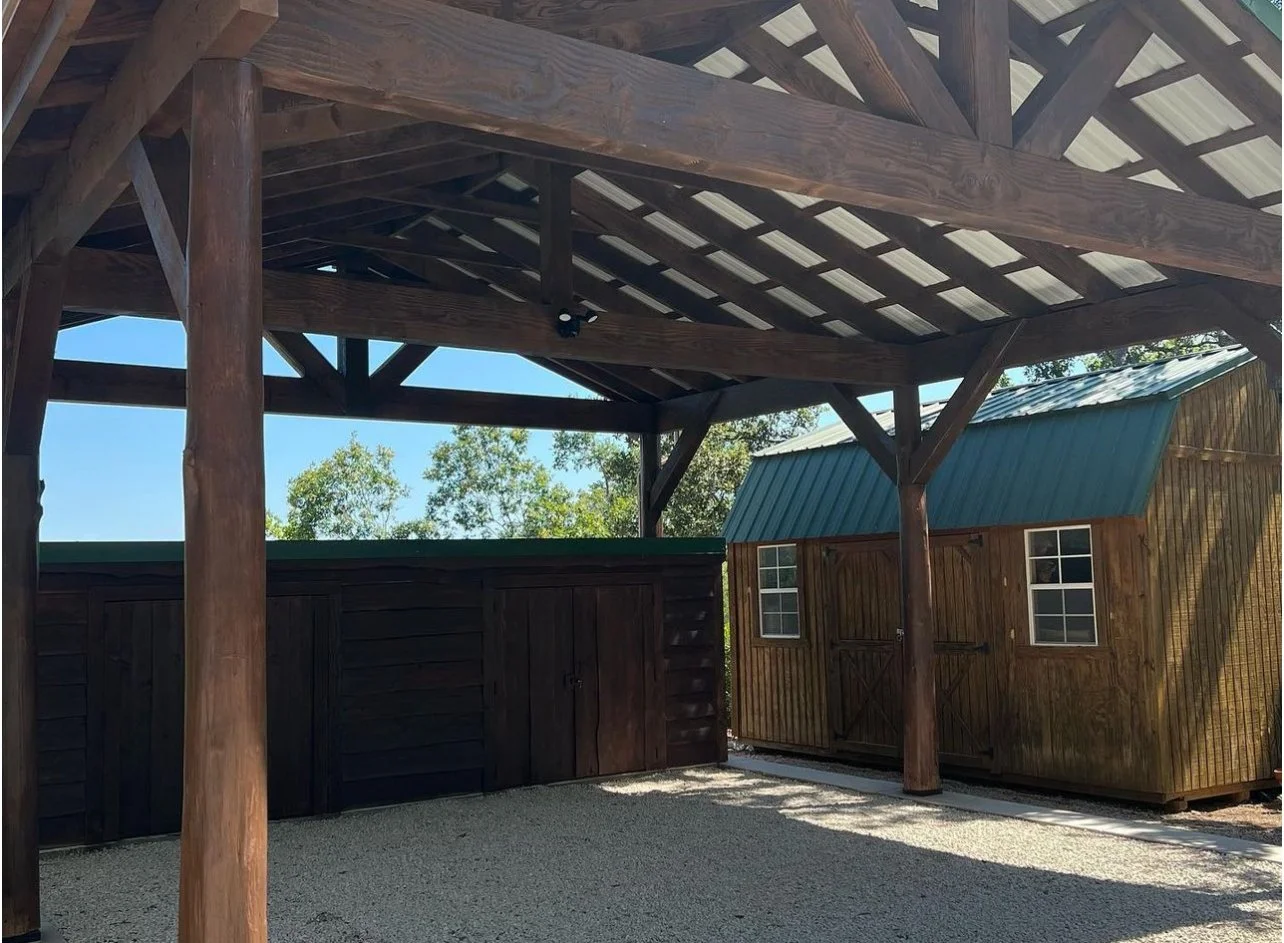 Timber-framed carport with exposed roof framing and a dark rear wall.