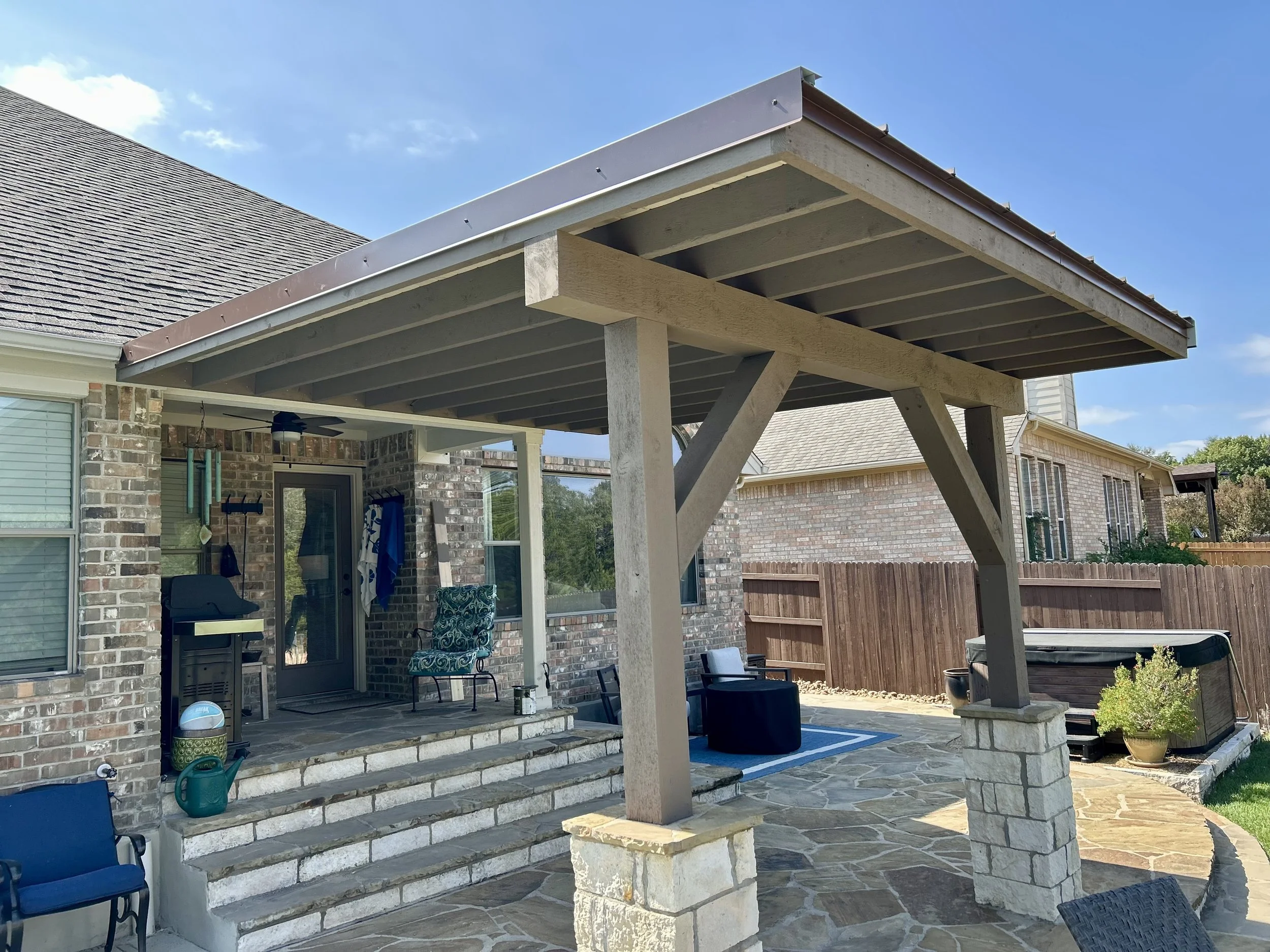 Covered patio with pitched roof, wood posts, and stone bases.