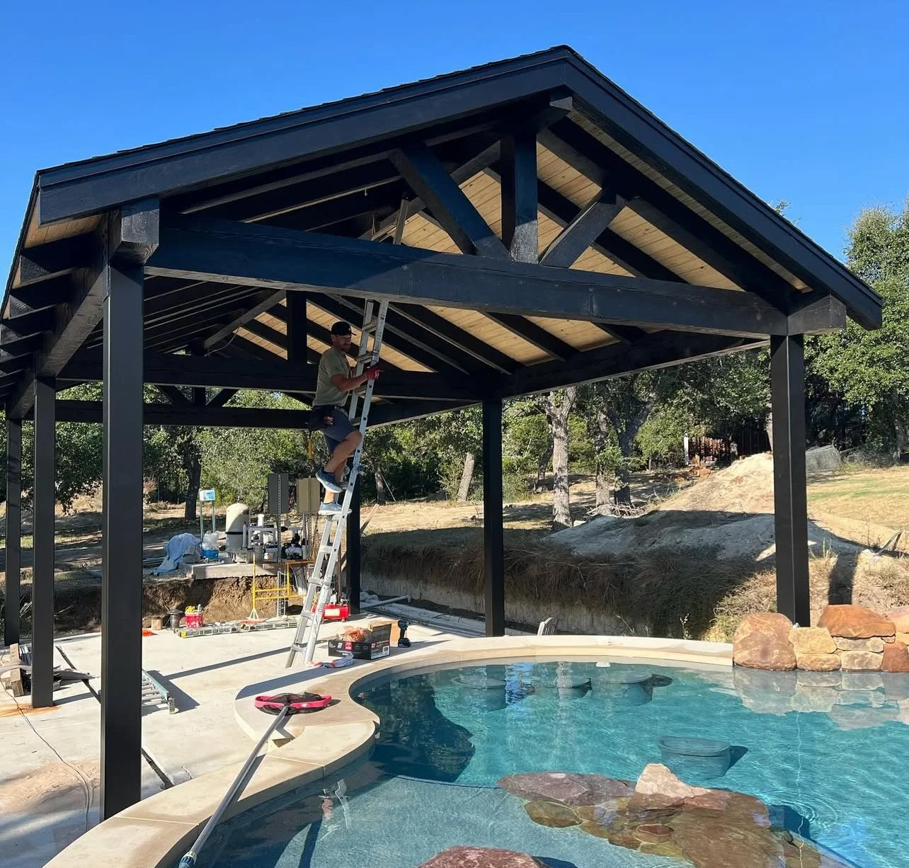Open-sided timber pavilion with a pitched roof beside a pool.