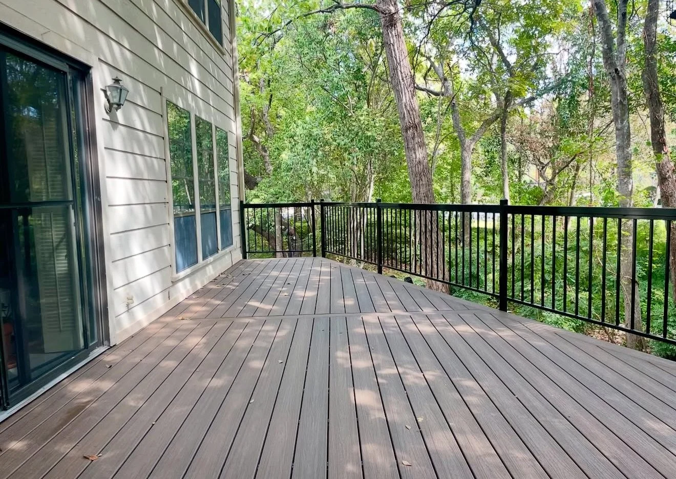 Deck alongside a house with black railing and wooded views.