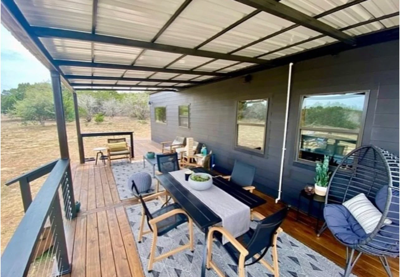Covered deck with outdoor dining table and seating beside a home.