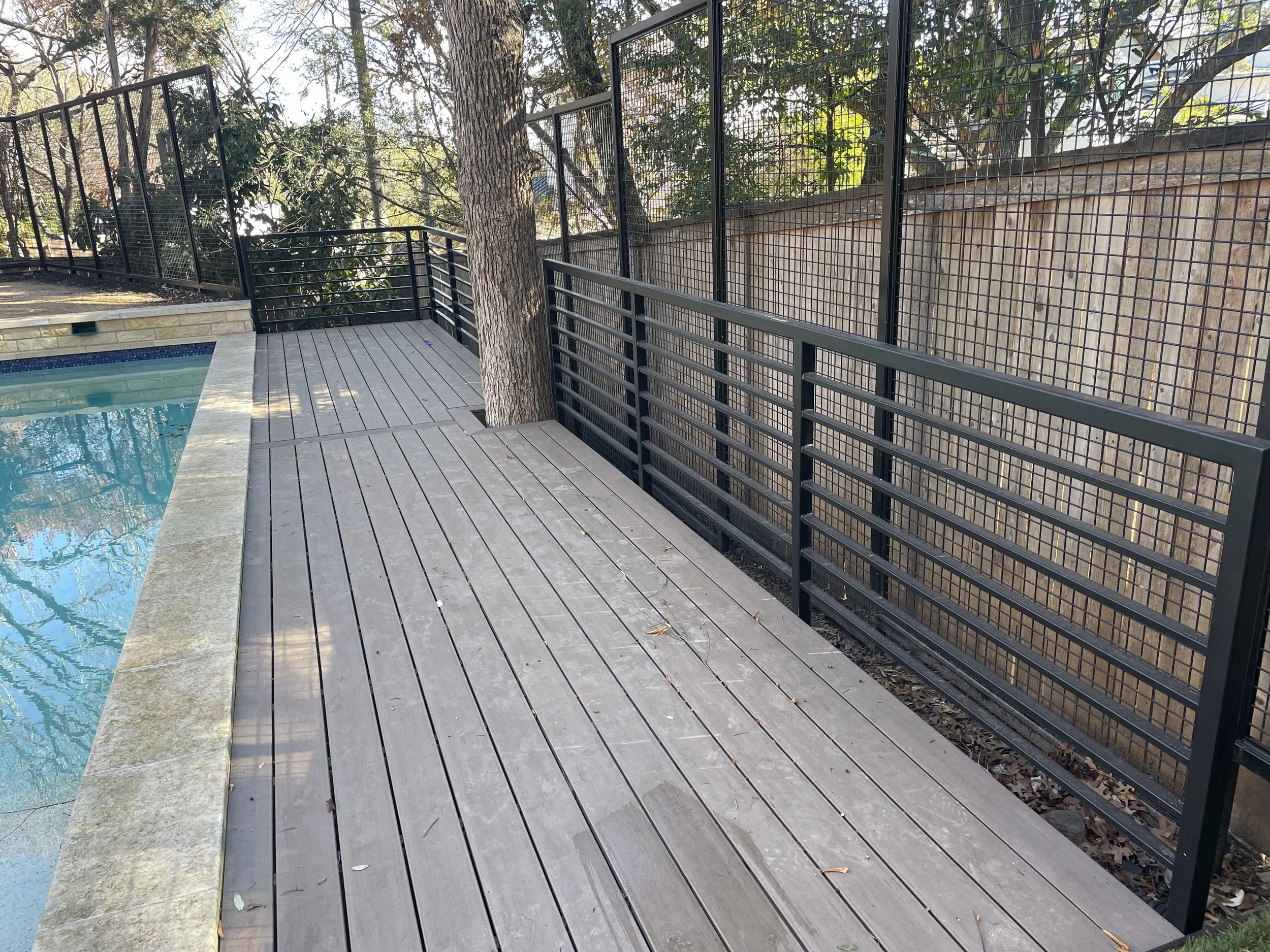 Gray deck with dark horizontal metal railing beside trees.