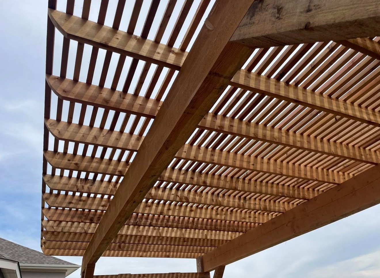 View beneath a wooden pergola with closely spaced overhead slats.
