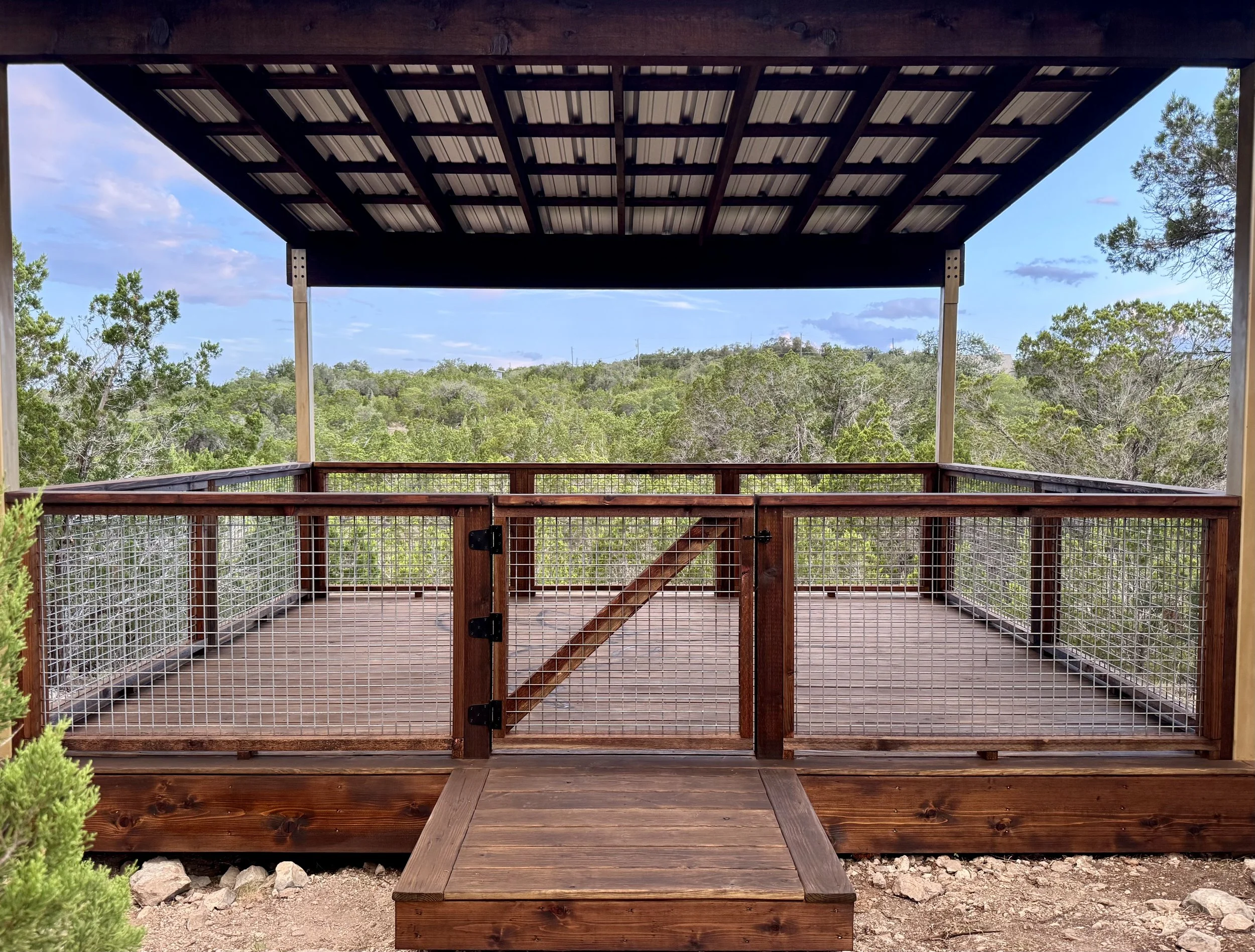 Wood deck with wire railing, a gate, and an overhead shade structure.