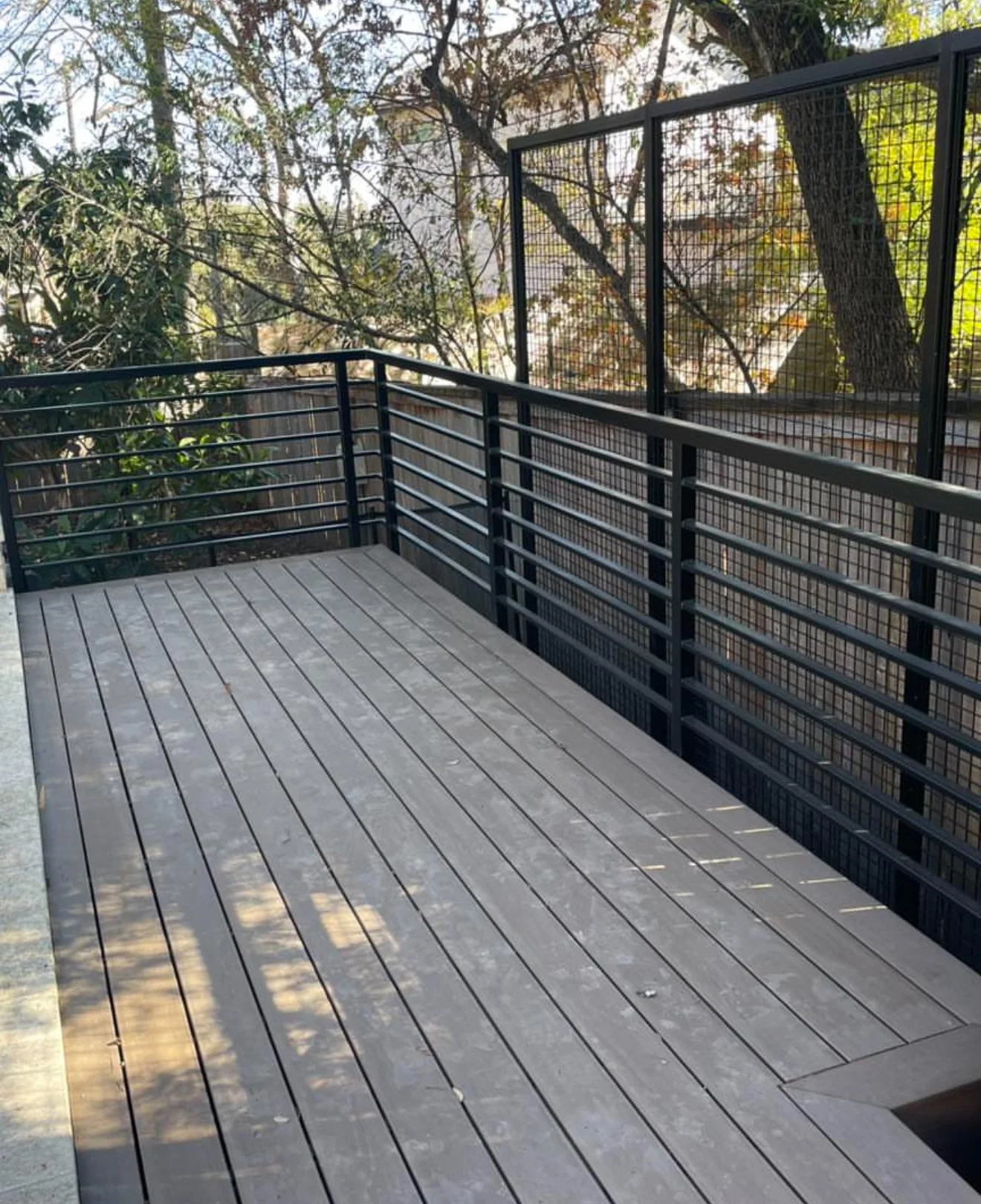 Gray deck with black horizontal metal railing among trees.