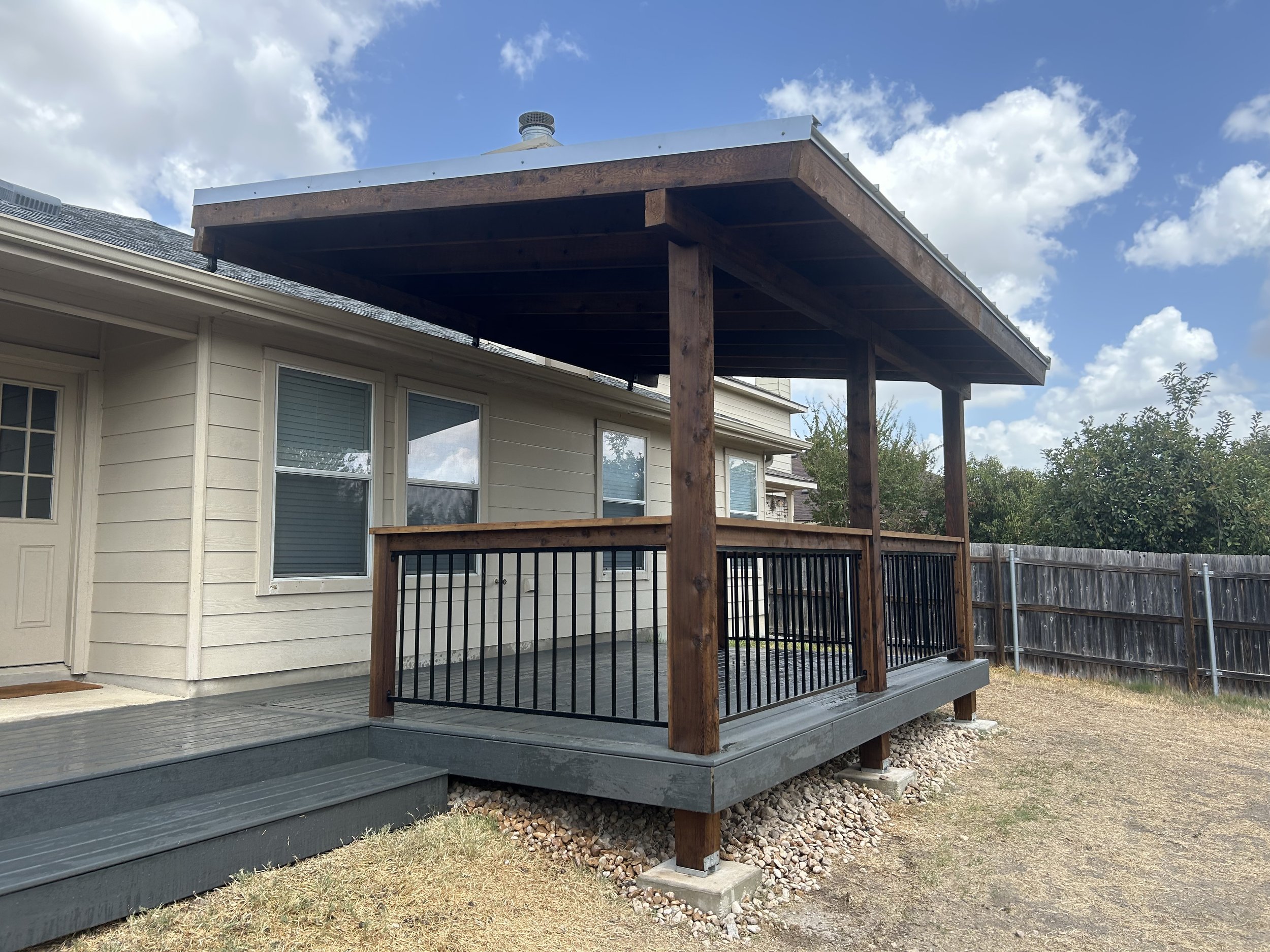 Covered deck with dark railing attached to a light-sided home.