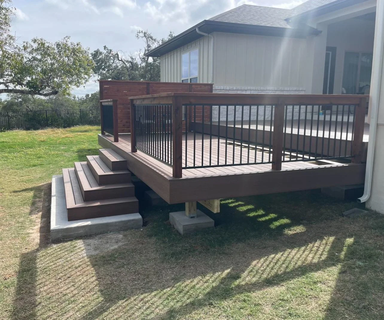 Raised deck with dark railings and wide steps next to a home.