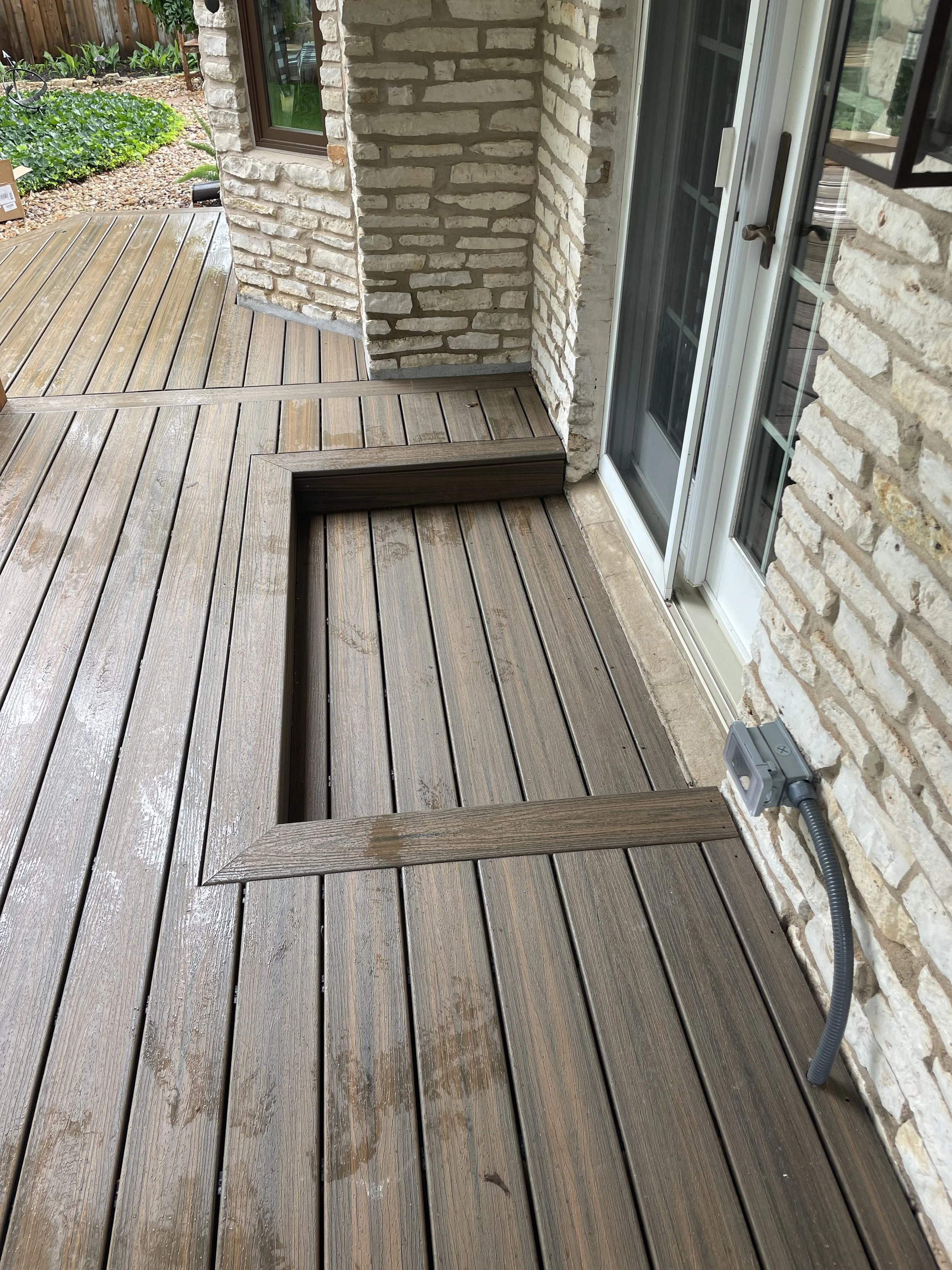 Wood decking beside a stone wall with a recessed section near a door.