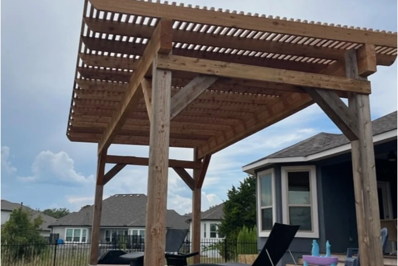 Freestanding wood pergola with slatted roof beside a house.