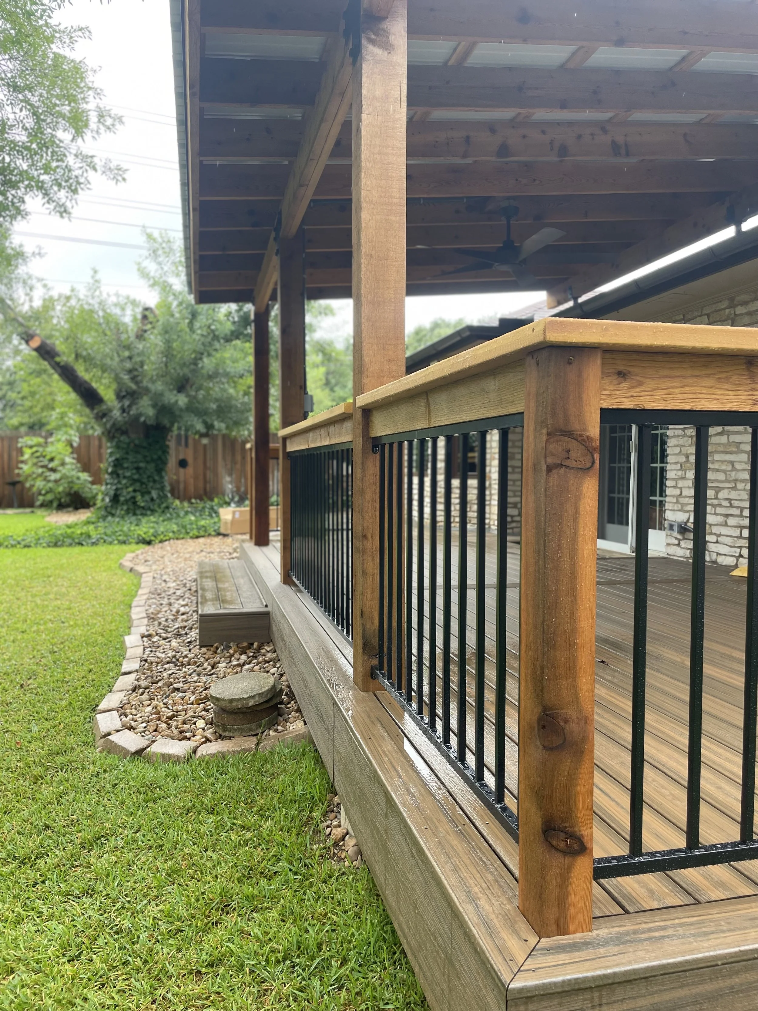 Covered deck with wood posts and black metal railing viewed from the yard.