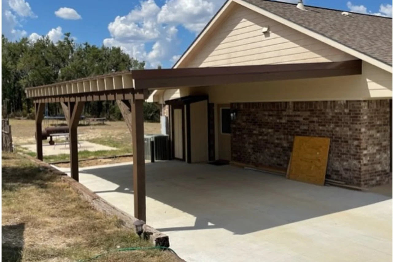 Wood pergola extending from a house over a concrete patio.