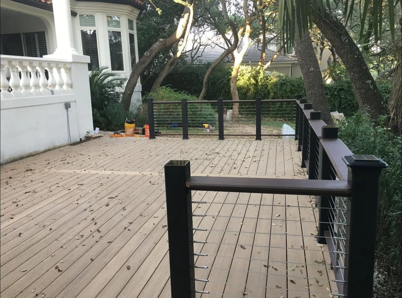 Large wood deck with dark posts and wire railing beside a house.