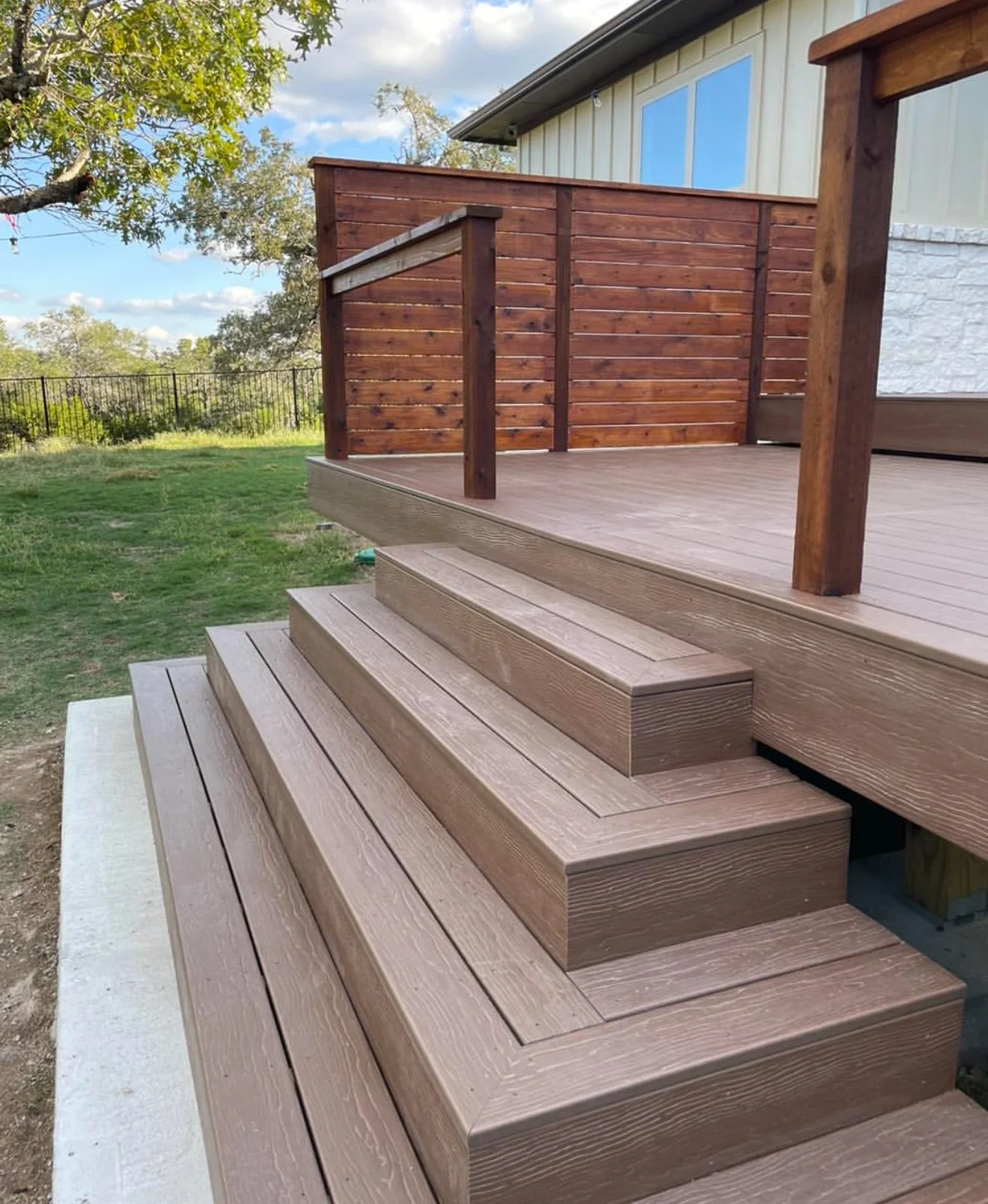 Wide deck steps leading to a raised landing with wood and metal railing.