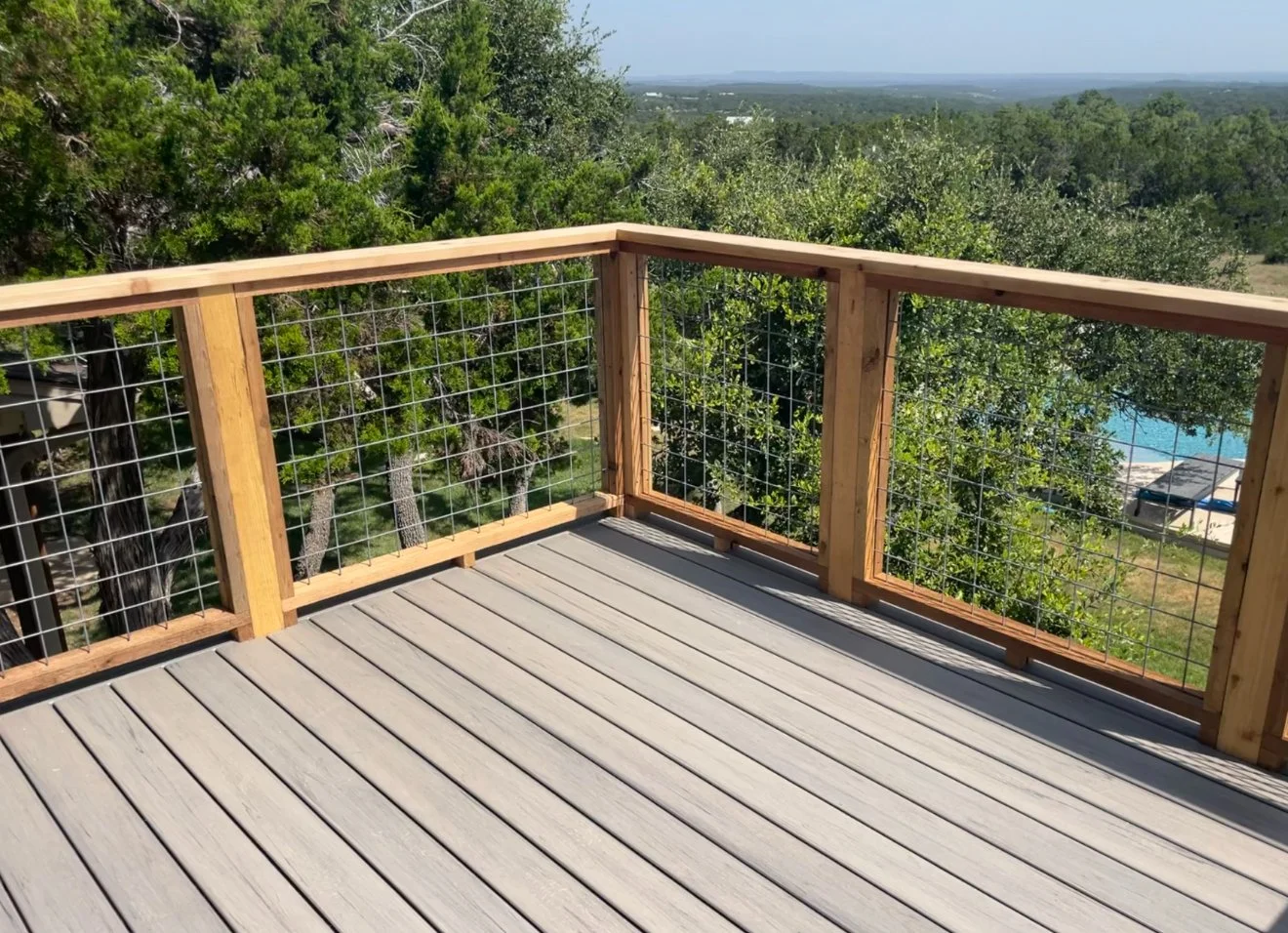 Deck corner with wood posts and black metal railing overlooking trees.