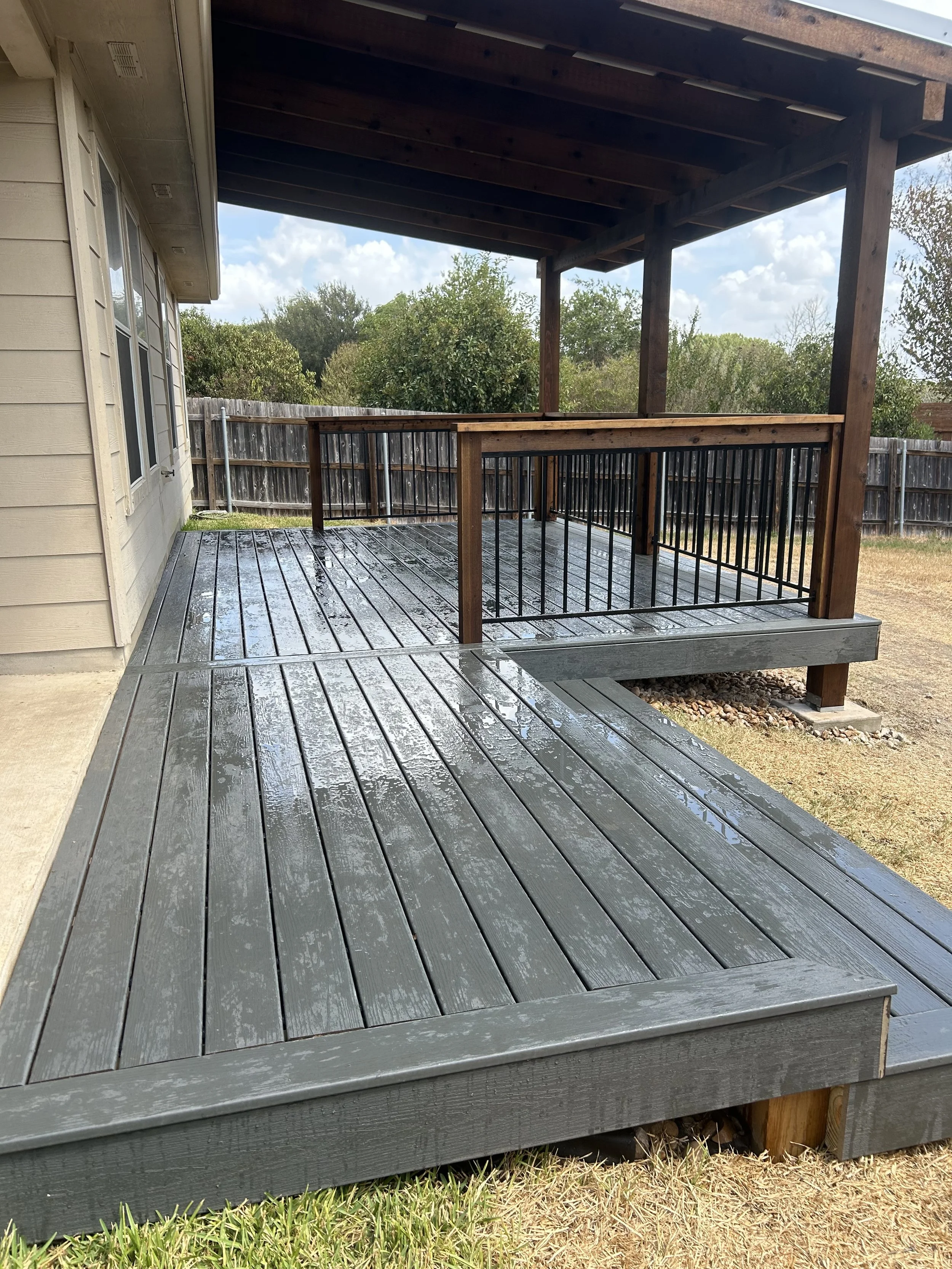 Gray deck boards and black metal railing beside a house.
