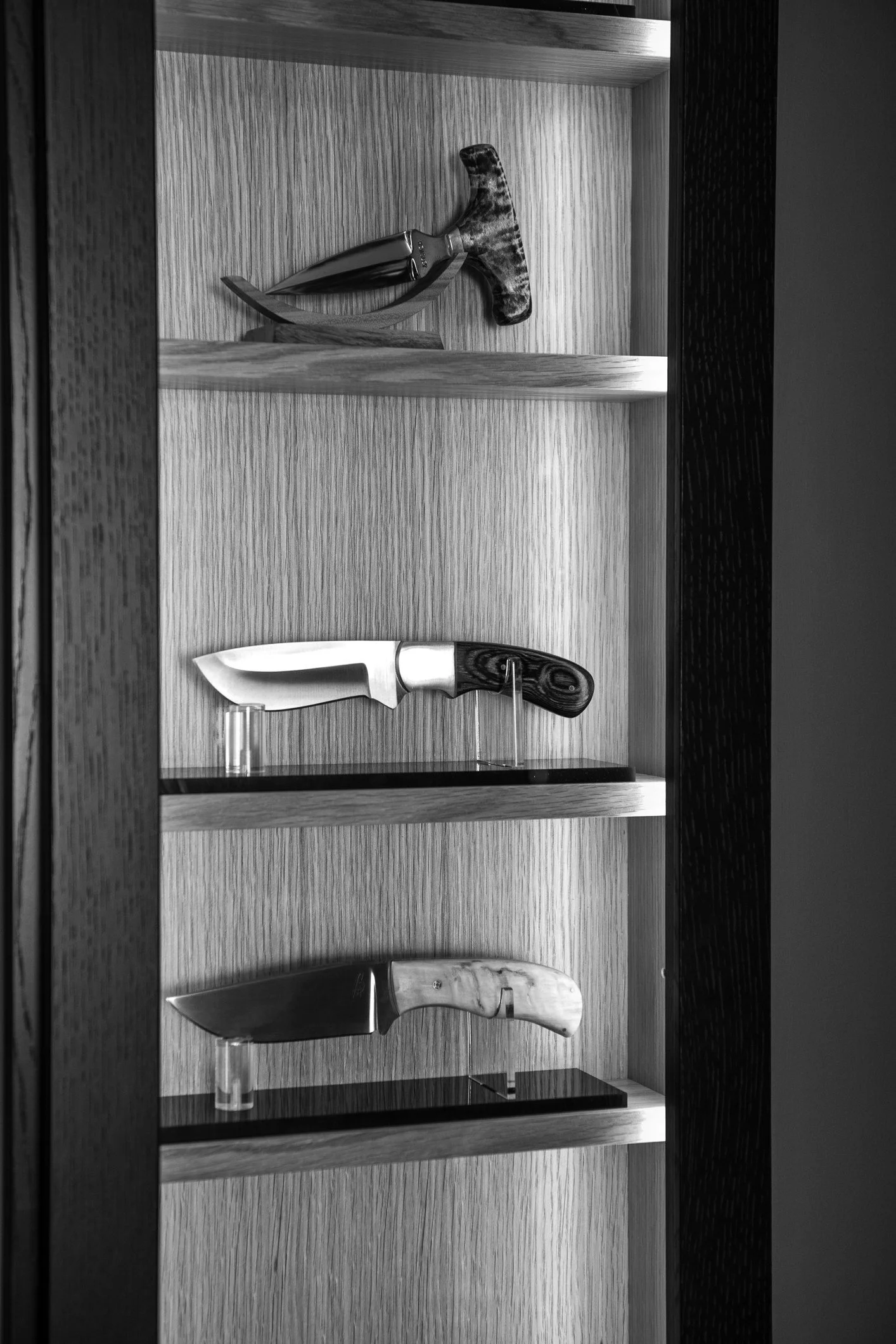 Display case with three knives on shelves, each with unique handles and blades, in black and white.
