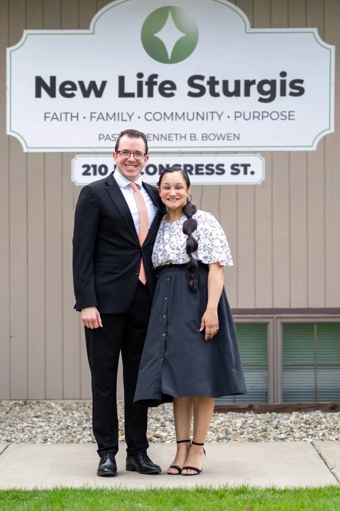 Two people standing in front of a church sign that reads 'Potter's House Church of Sturgis, Pastor Brian M. Bowen, A United Pentecostal Church.' The man is in a suit and the woman in a skirt and blouse, both smiling.