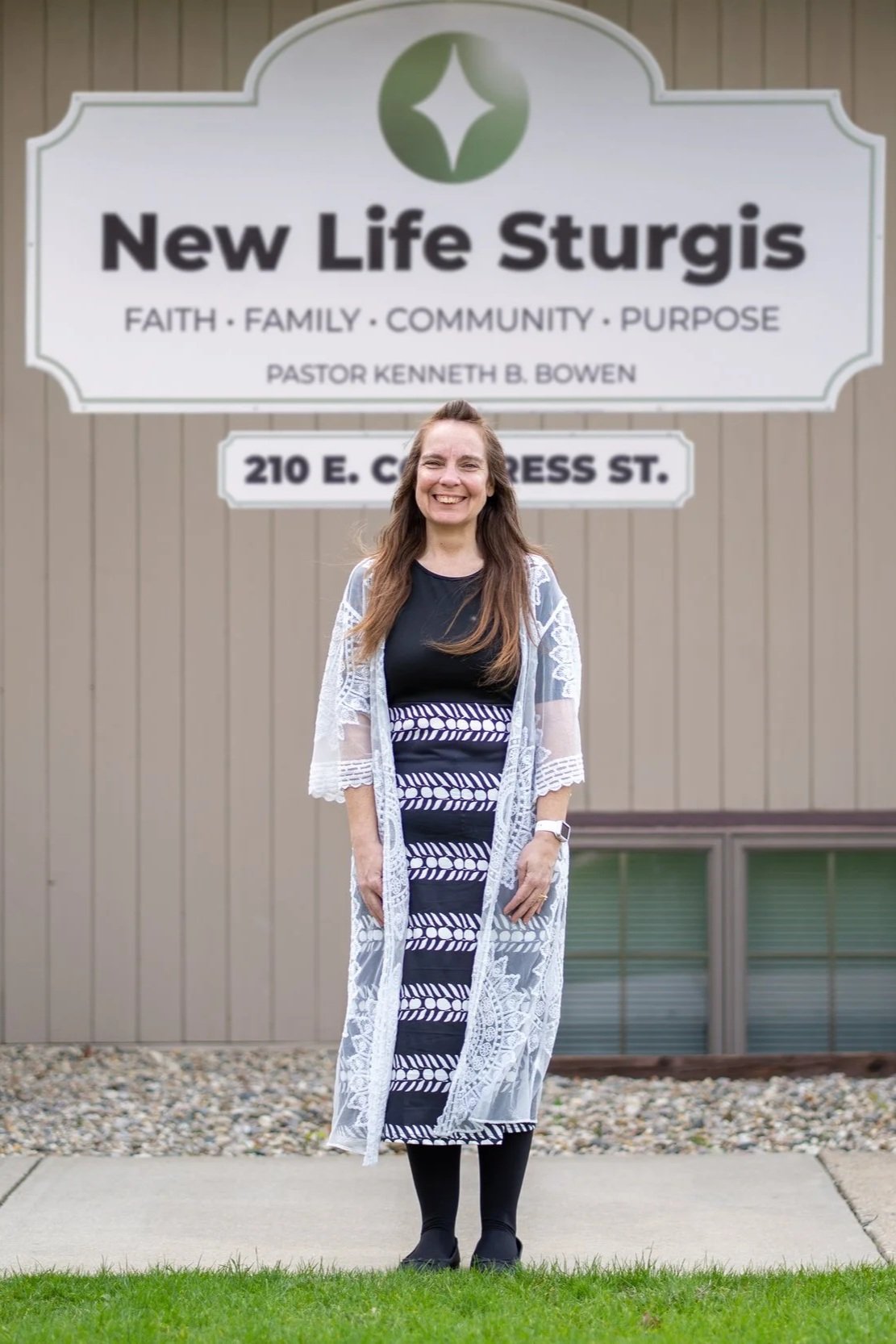 Woman standing in front of Potter's House Church of Sturgis sign, wearing a black and white outfit with a lace shawl.