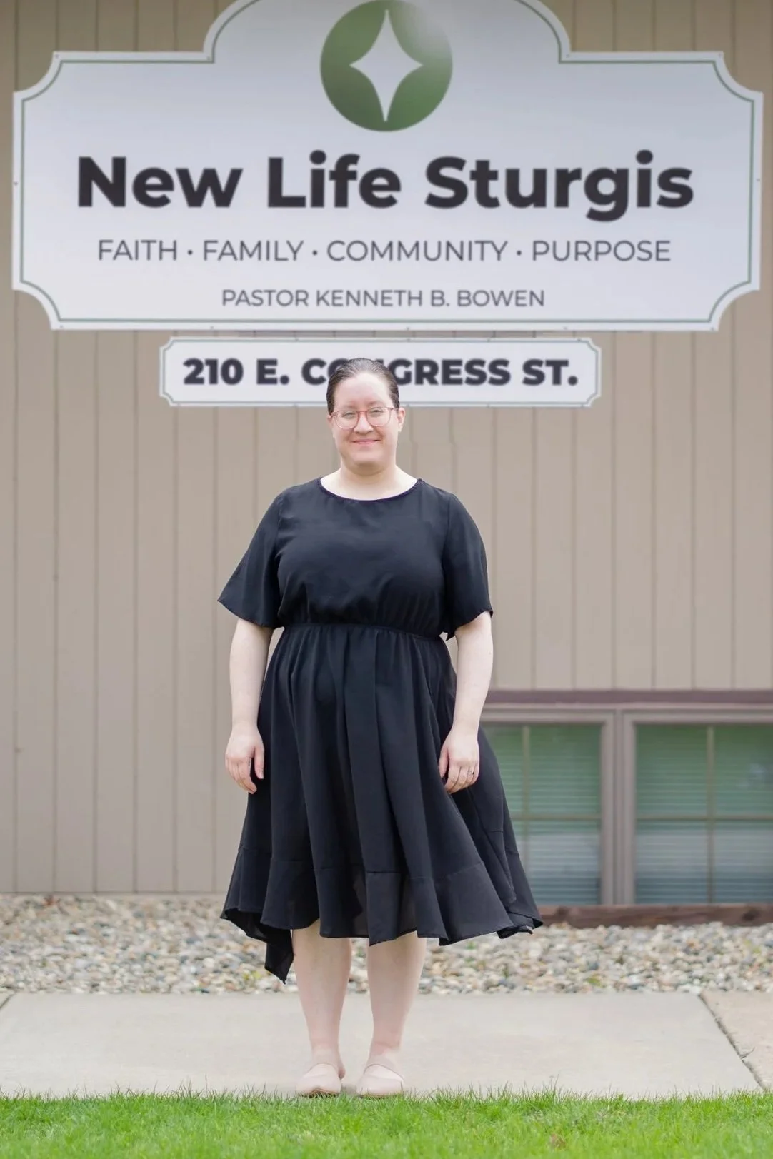 Person in a black dress standing in front of a church sign for Potter's House Church of Sturgis, located at 210 E. Congress St.