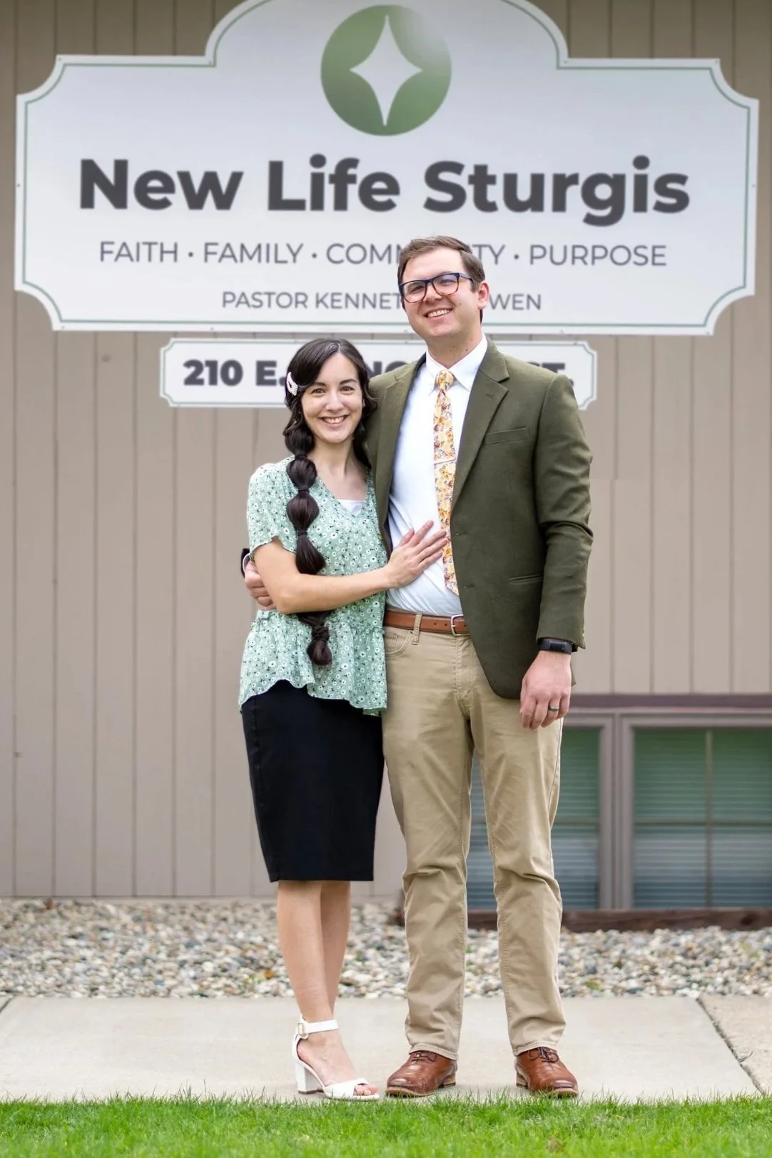 A man and woman smiling, standing in front of a sign for Potter's House Church of Sturgis.