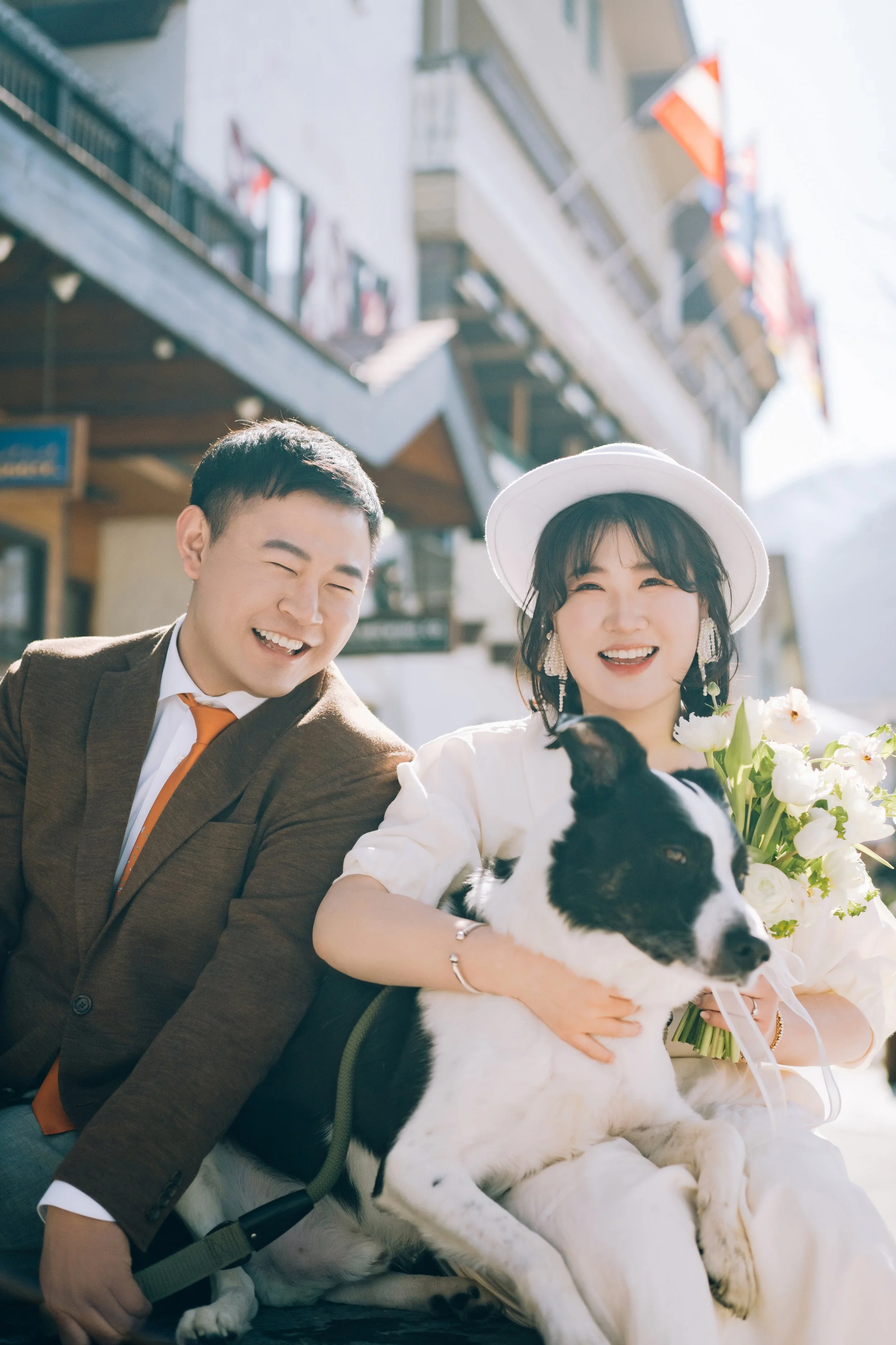 Smiling couple with a dog and flowers on a sunny street in a European town.