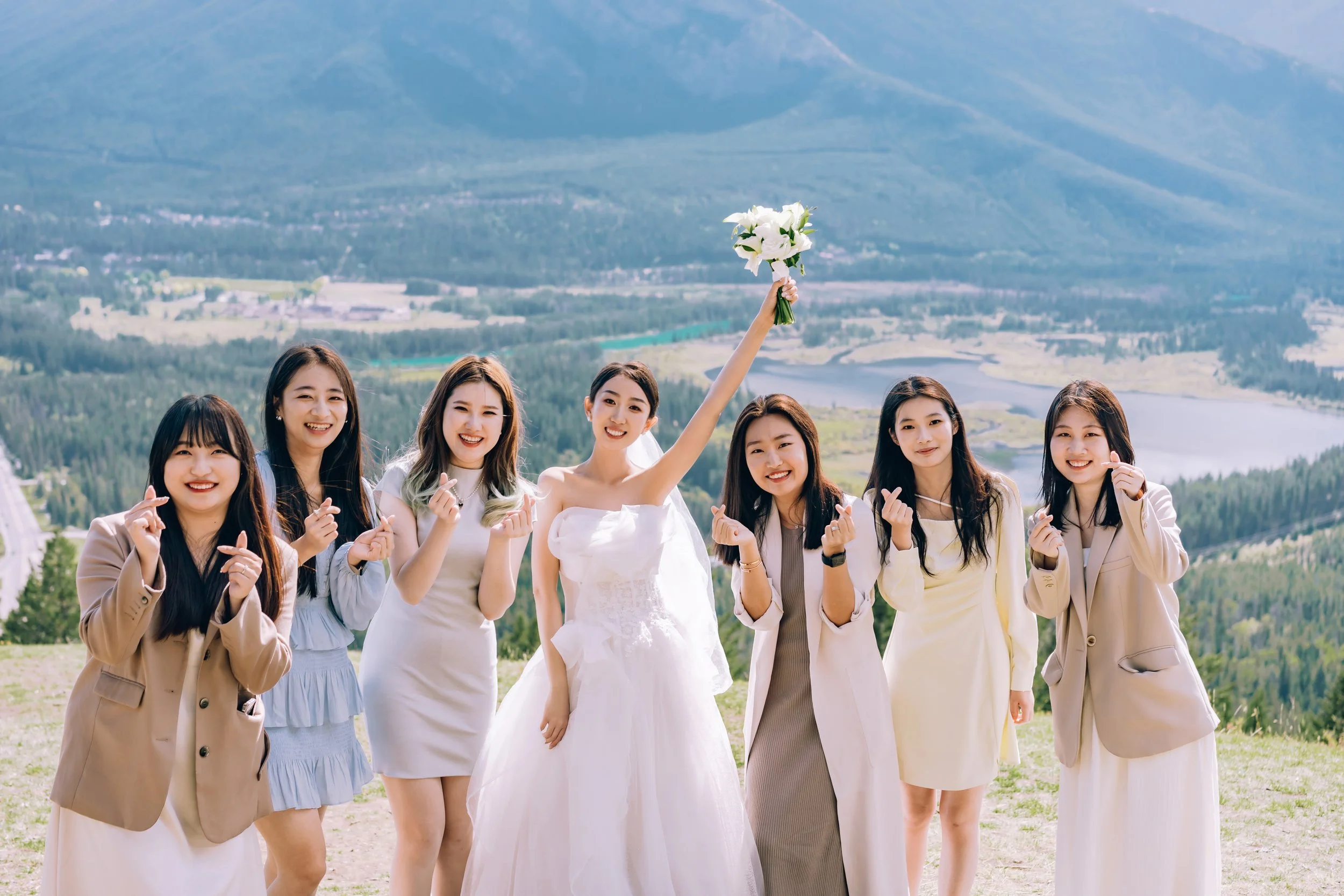 Group of women at outdoor wedding, one holding bouquet, scenic mountain and lake backdrop.