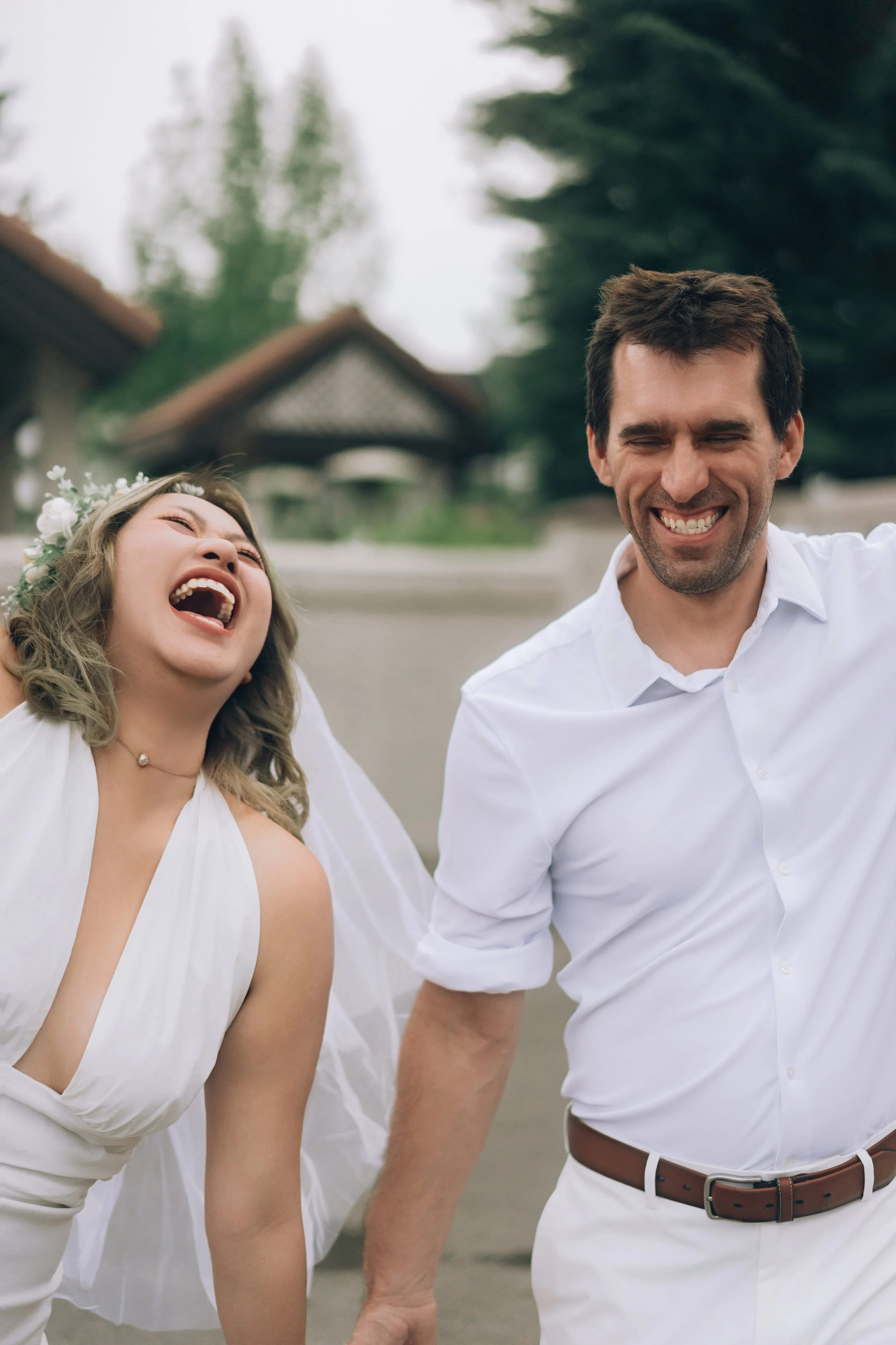Bride and groom laughing outdoors in wedding attire