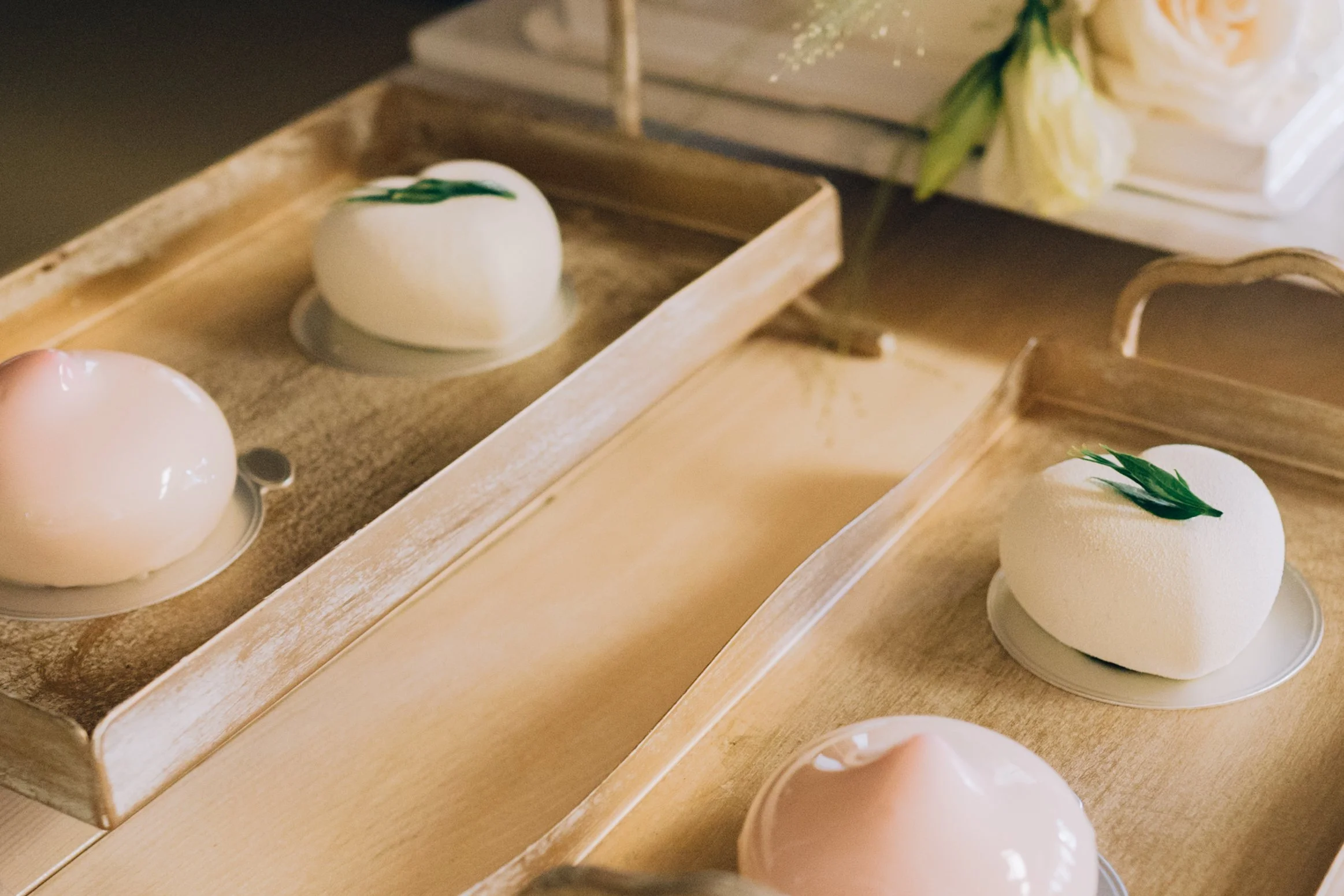 Elegant white desserts with green garnish on white plates, arranged on wooden trays.