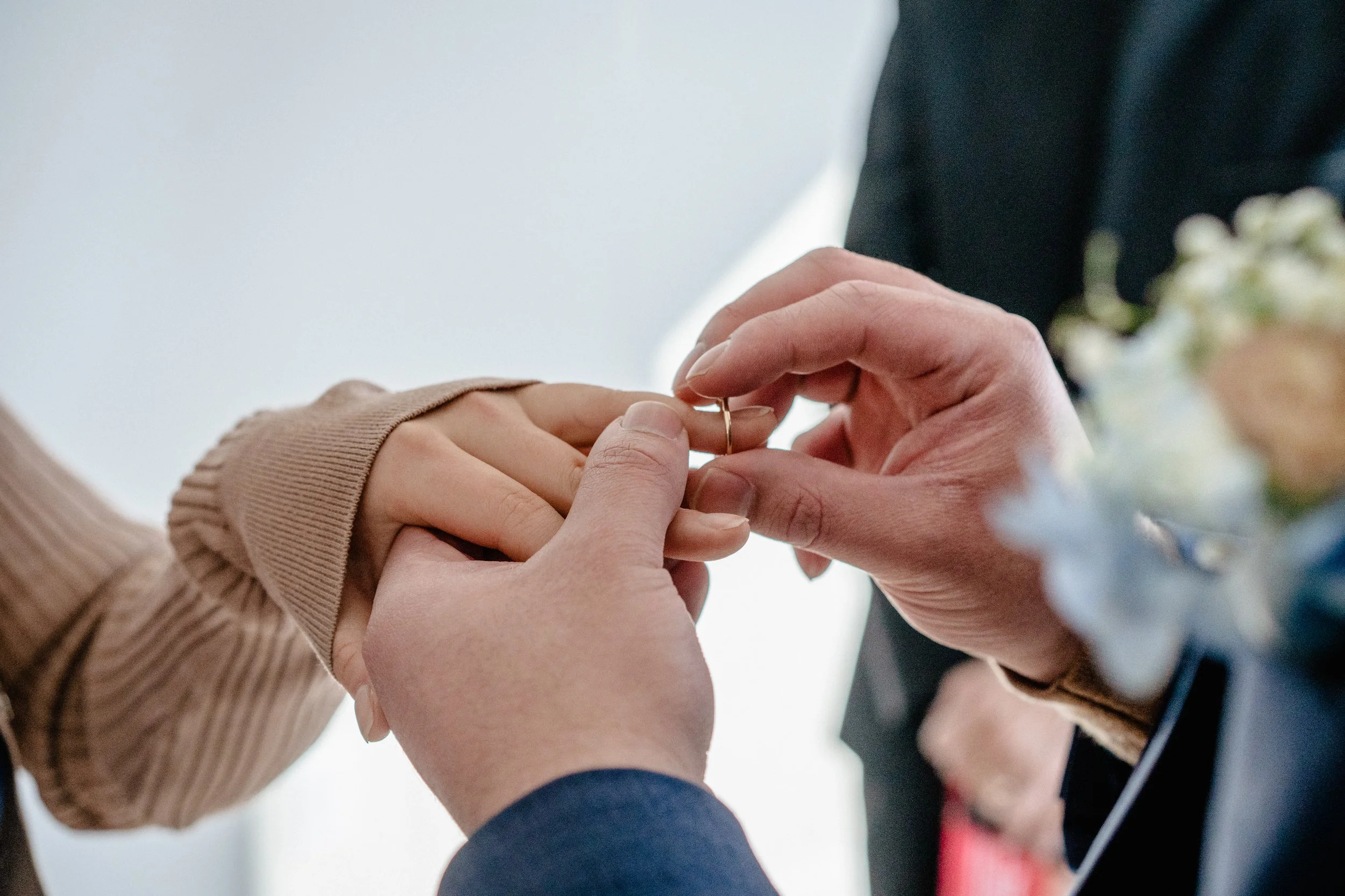 A person is placing a wedding ring on another person's finger during a wedding ceremony.