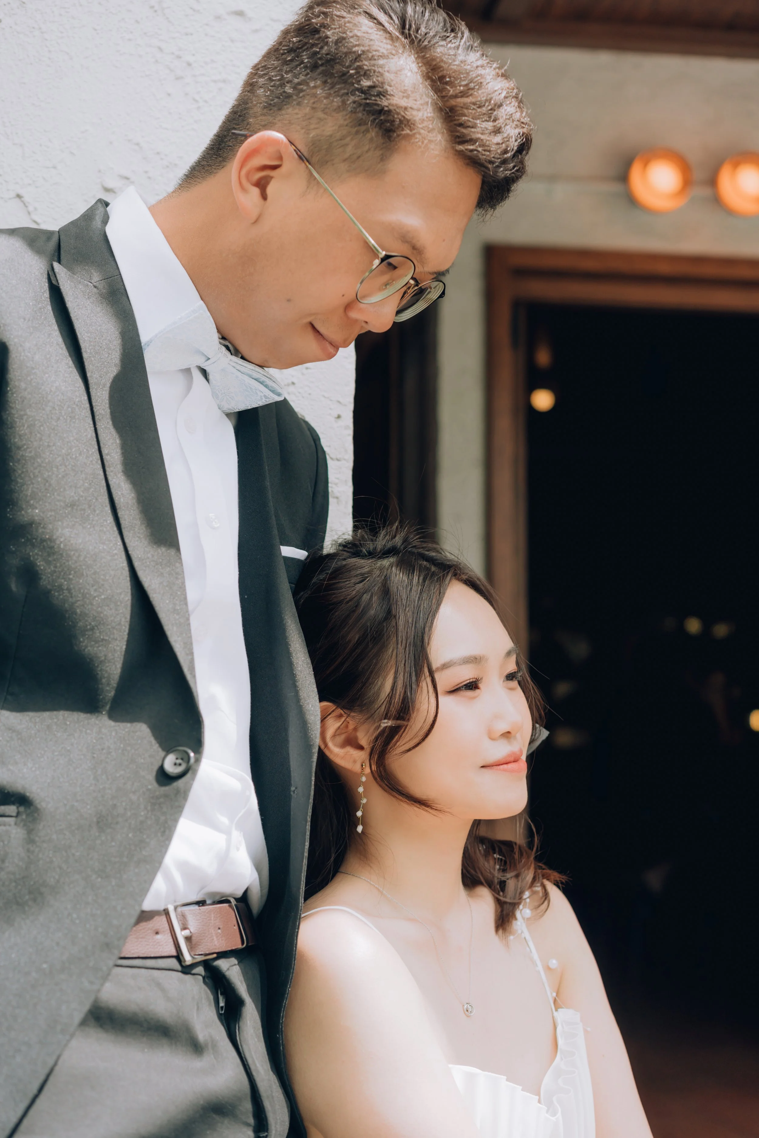 A man in a tuxedo leaning towards a woman in a white dress, both smiling and enjoying a moment together at an event.