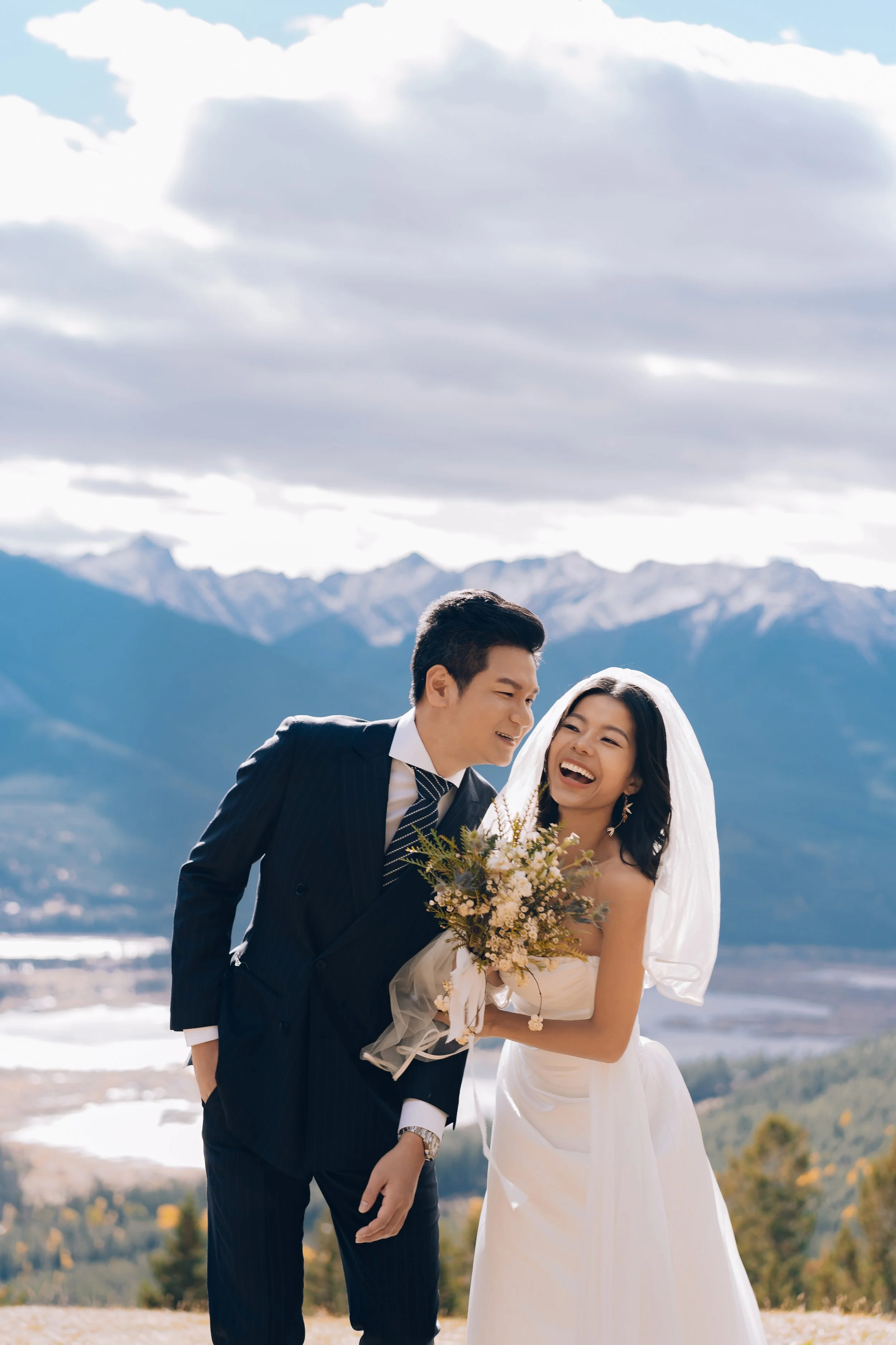 A bride and groom sharing a joyful moment outdoors, with mountains in the background, during their wedding celebration.