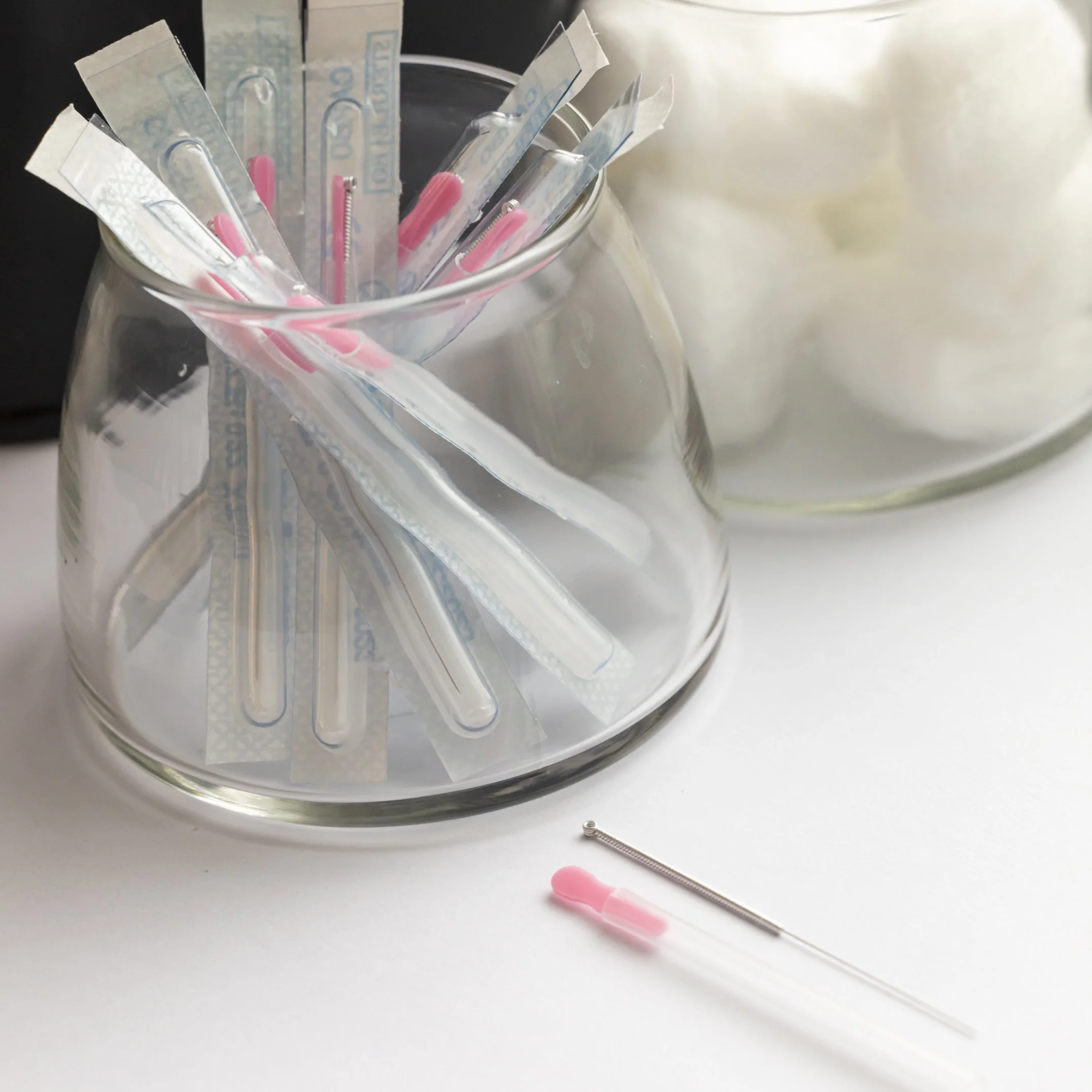 An open acupuncture needle is pictured beside its plastic tube. In the background a set of acupuncture needles are in a glass dish, and another glass dish holds cotton balls. Acupuncture, Bruce Village Chiropractic