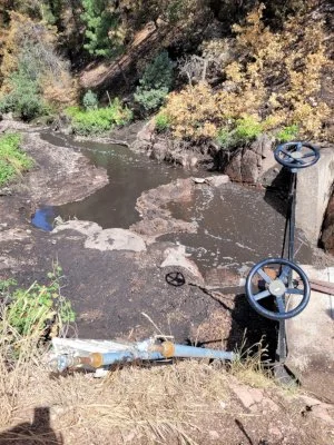 Picture shows the finished look of the BWWD Weir with creek water hugging the side next to the large boulders with the Infiltration Gallery underneath the gravel/sand with ash on top.