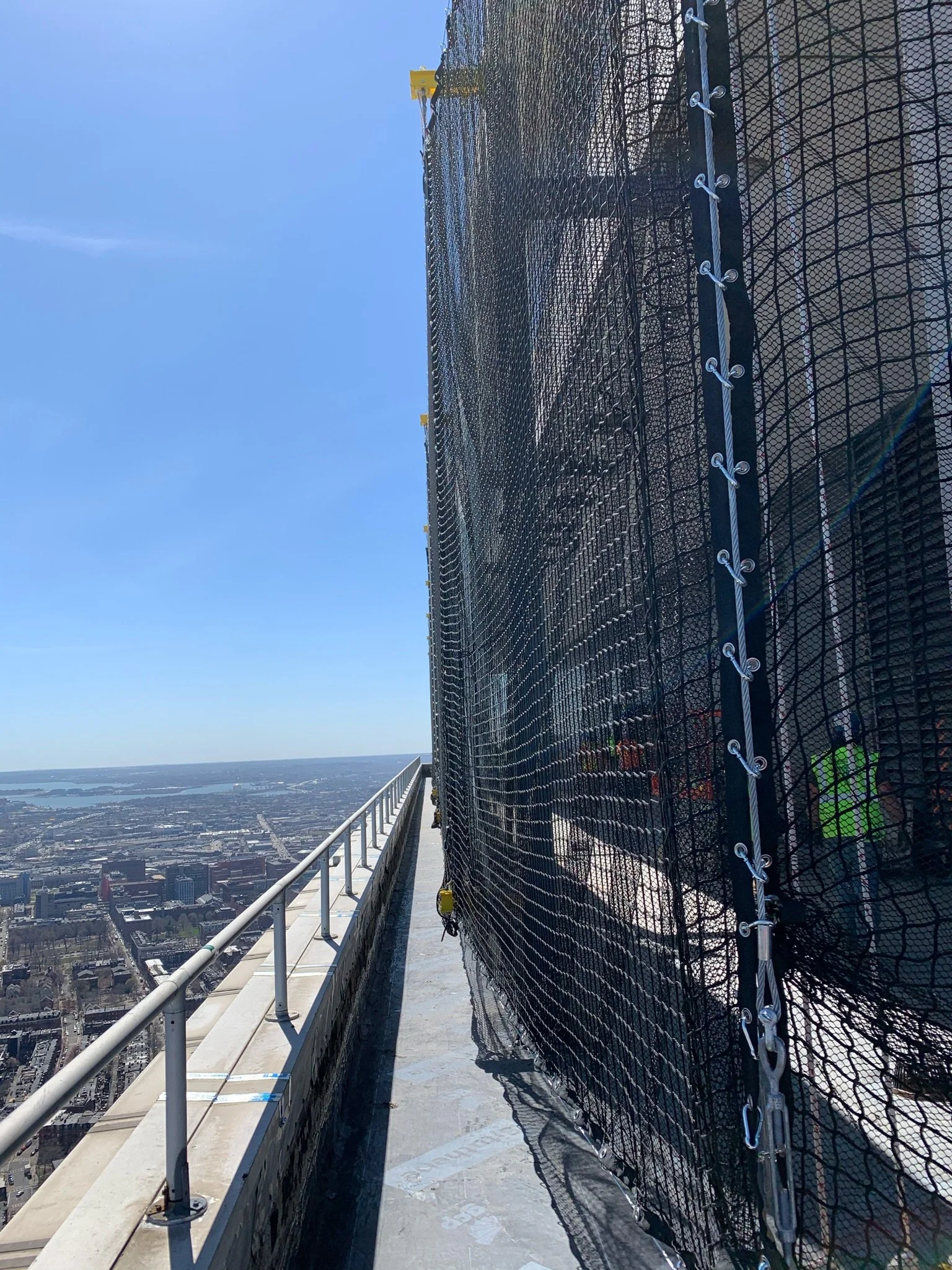 Engineered debris containment netting system installed on multi-level structural steel building for high-rise renovation and retrofit projectground.