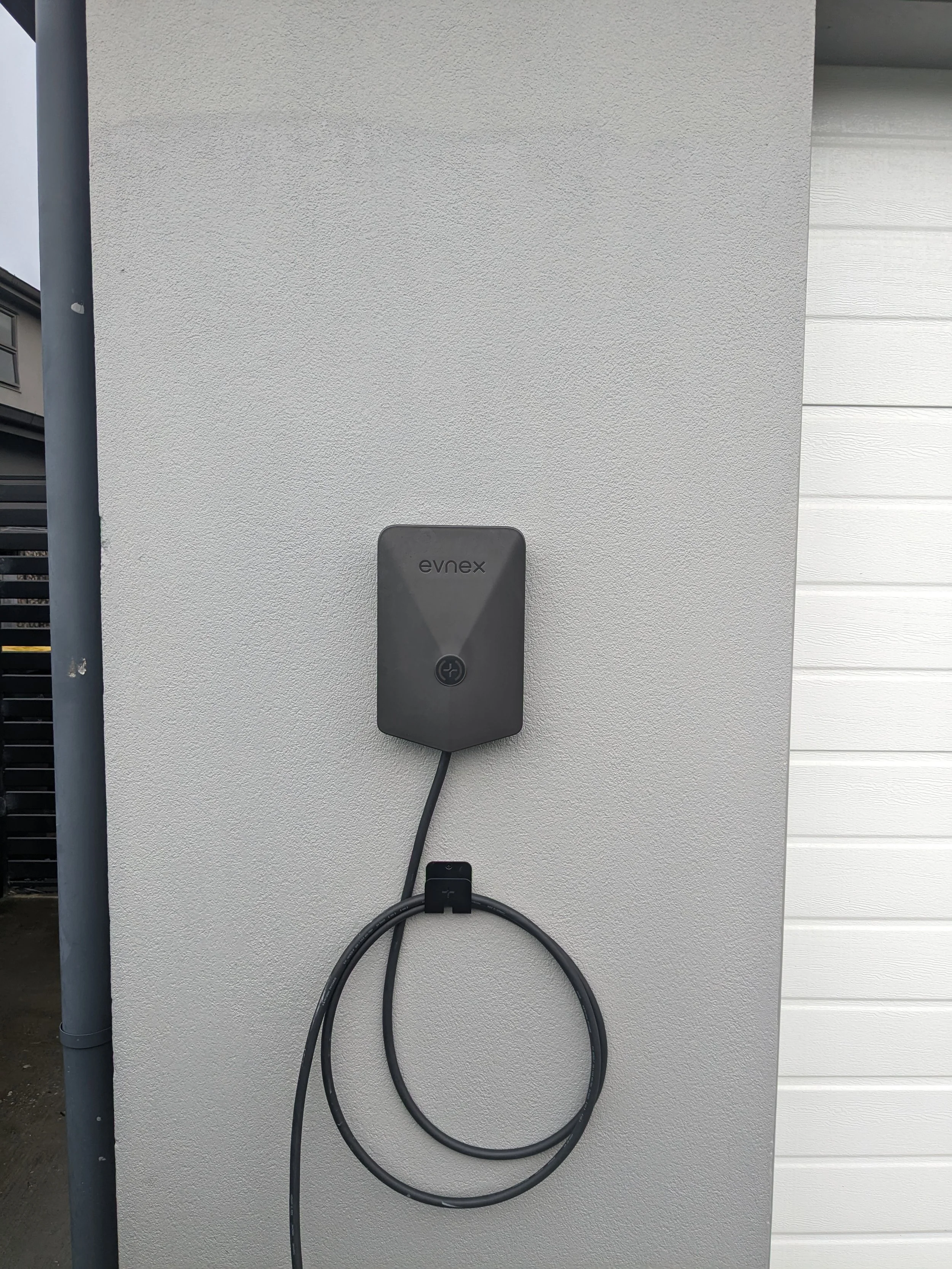 Electric vehicle charging station on an exterior wall of a building, with a charging cable hanging from it.