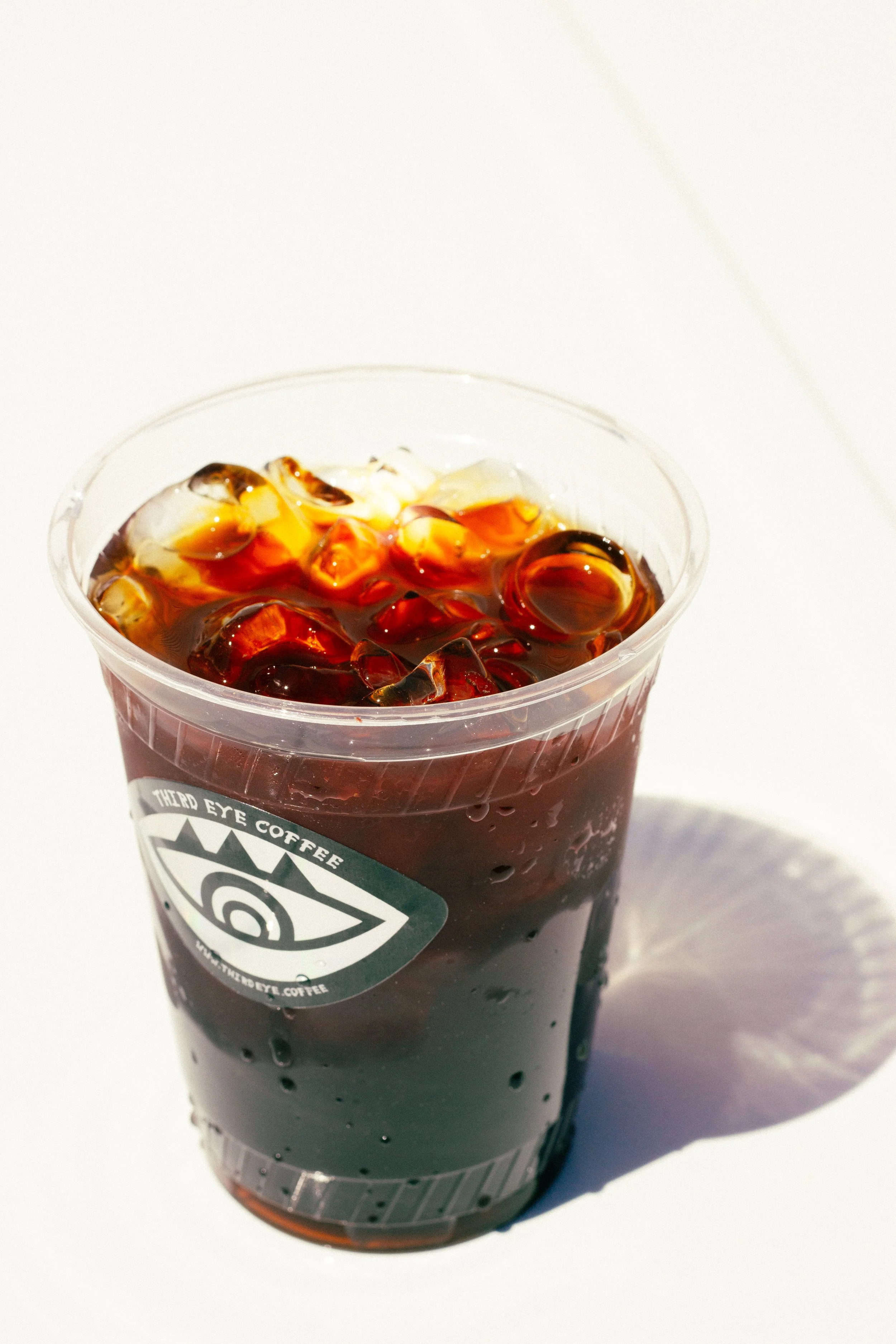 Plastic cup filled with iced coffee and ice cubes, topped with a logo of The Odd Eye Coffee.