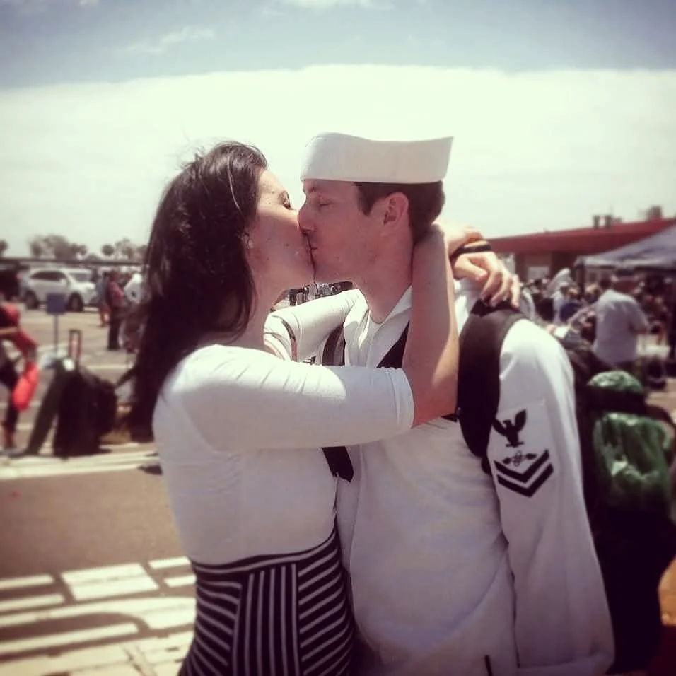 A woman and a man in a Navy uniform kissing at an airport.