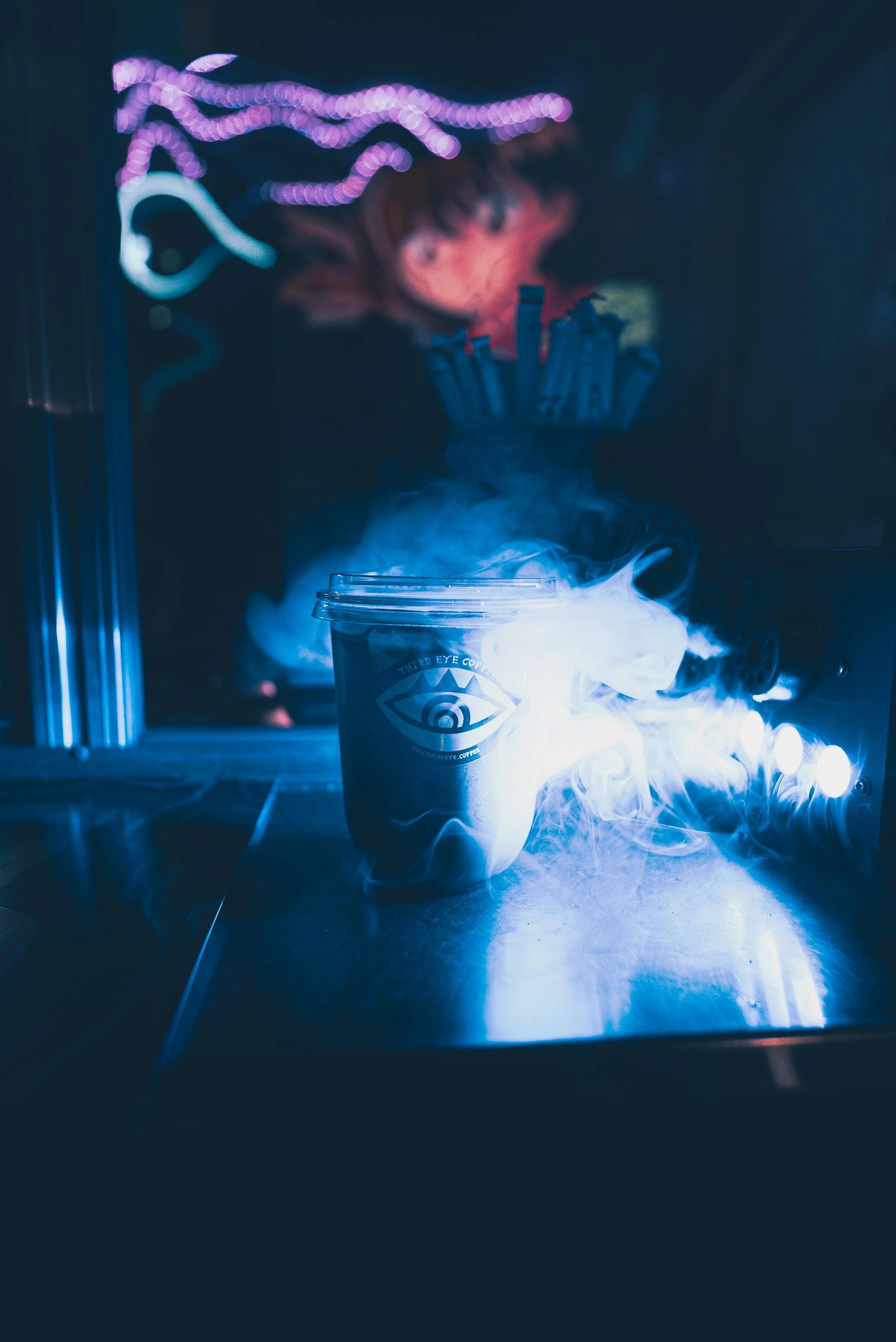 A steaming coffee cup with the logo 'Third Eye Coffee' on a metallic surface, with a background of colorful neon lights.