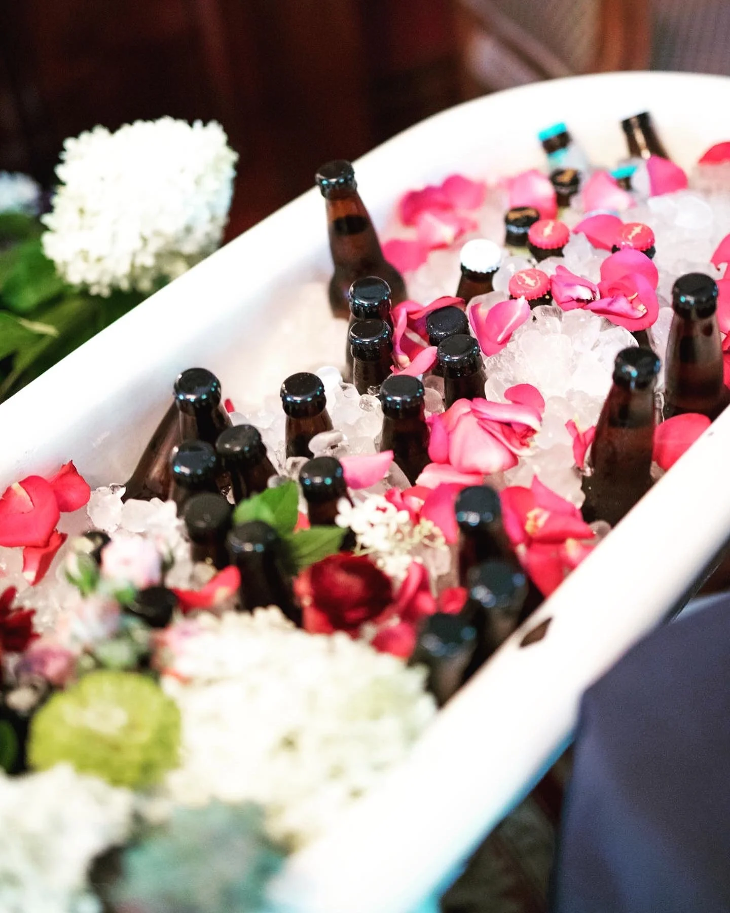 Bottles in ice-filled bathtub with pink petals and flowers.