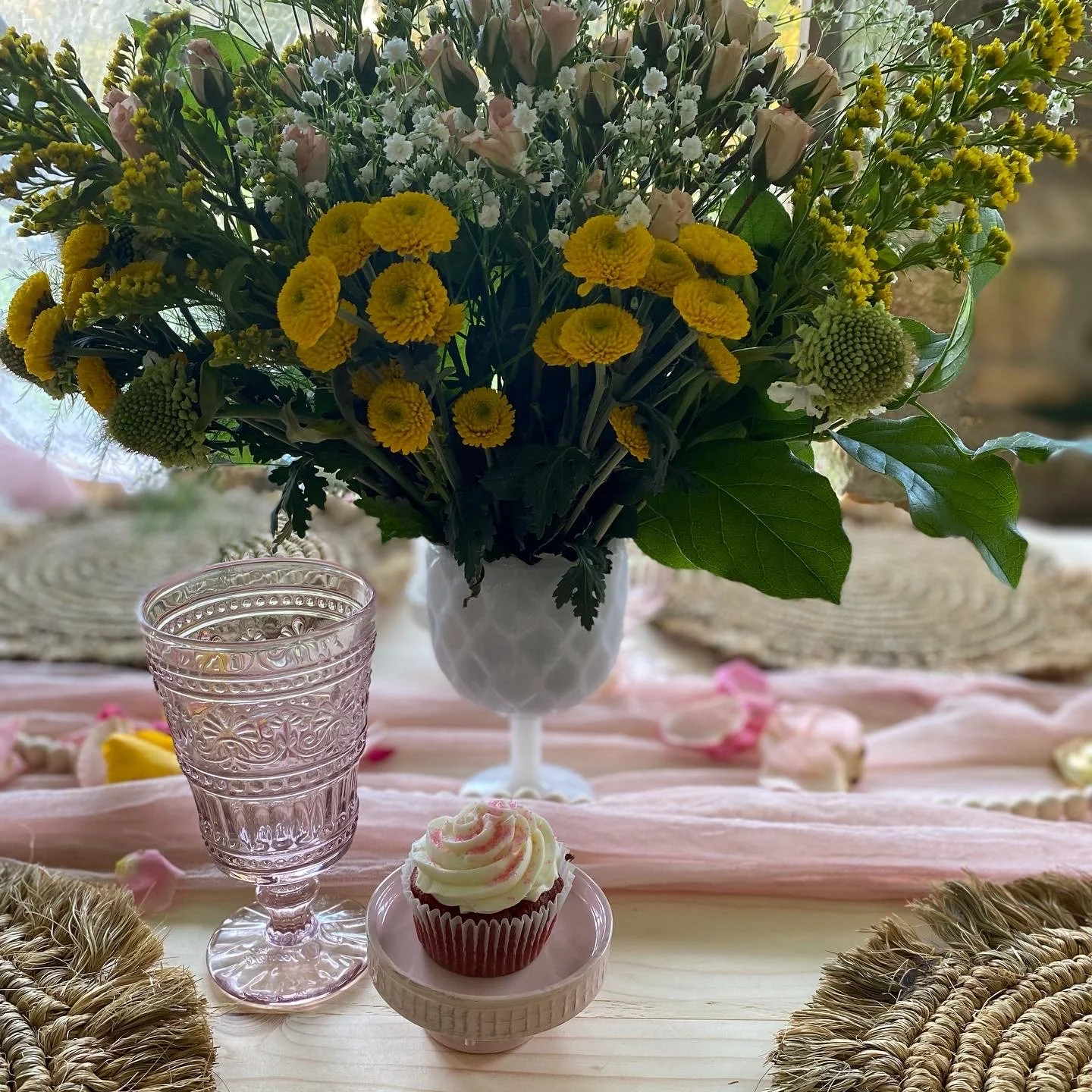 Table setting with a floral bouquet, pink goblet, and cupcake