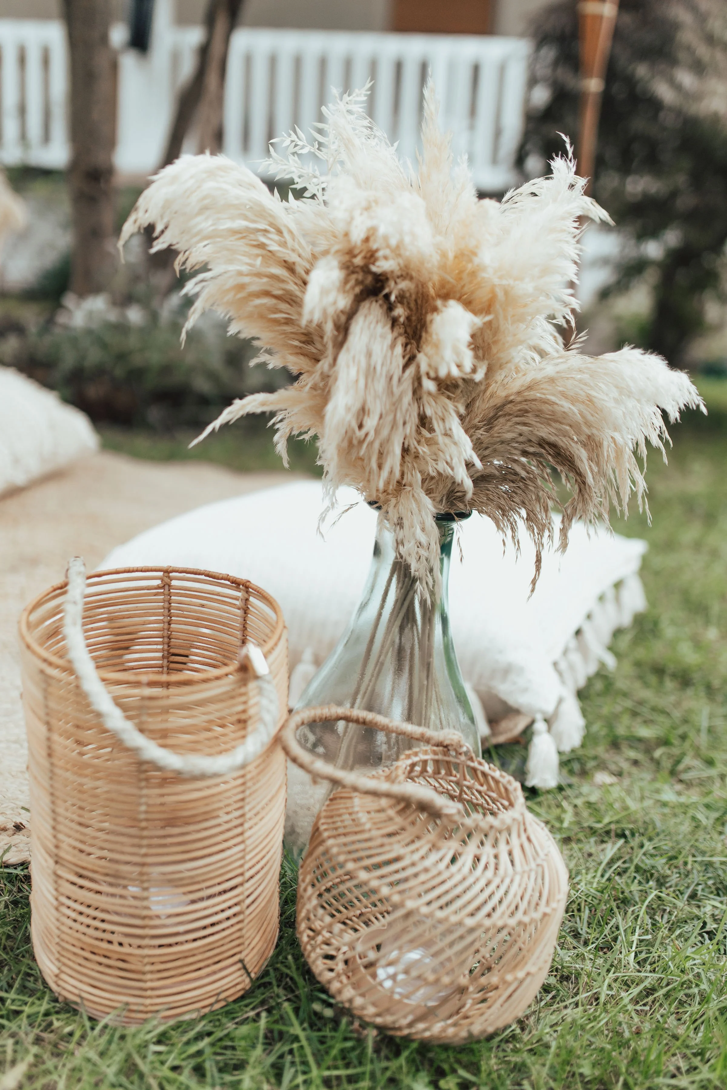 Outdoor picnic setup with pampas grass in a glass vase and wicker baskets on a lawn.