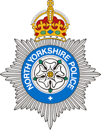 North Yorkshire Police badge with a crown on top, a silver star-shaped medal, and a blue and white circular emblem with a white rose and the text 'North Yorkshire Police'.