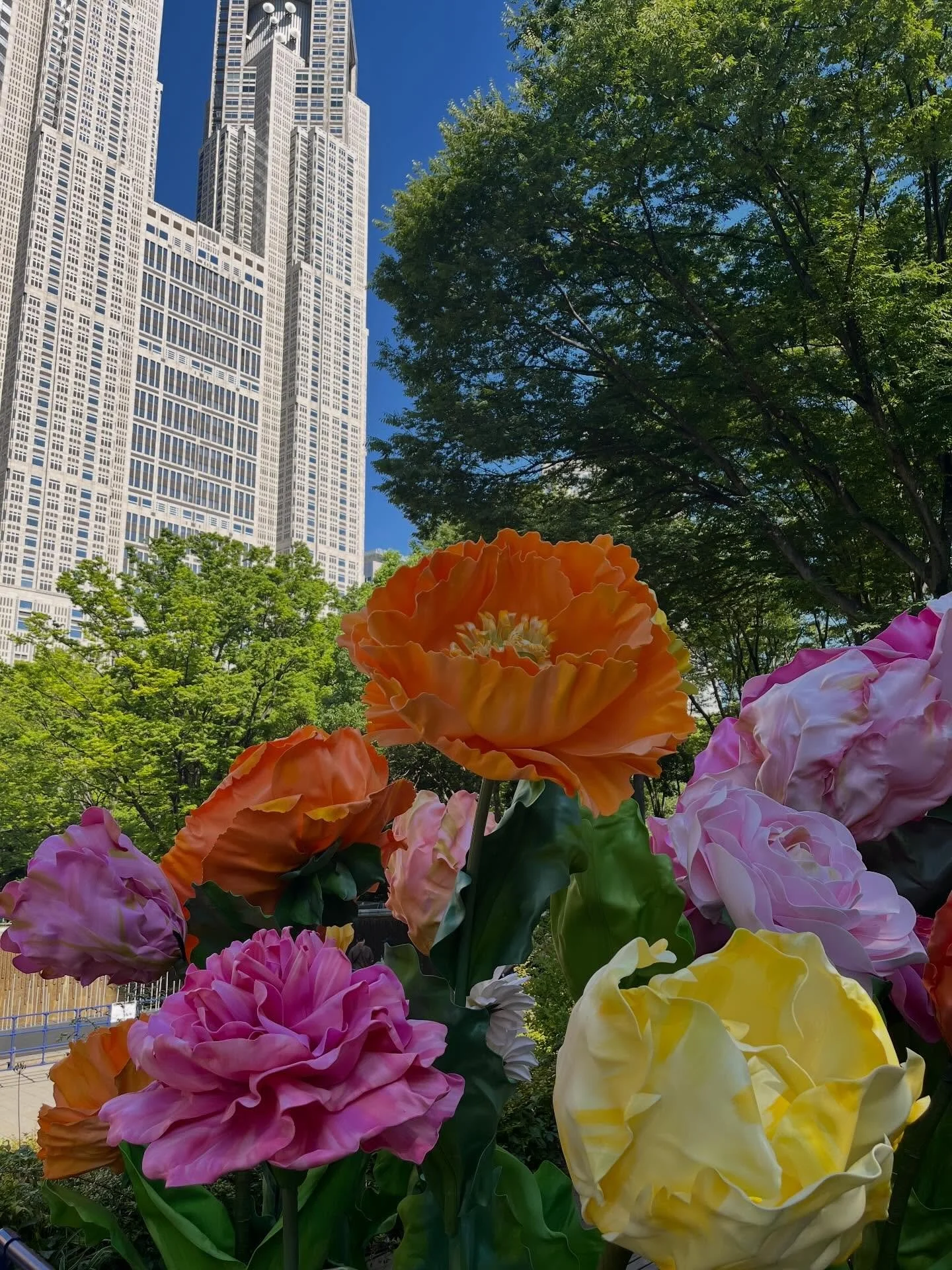 Giant flowers by @megu_petaldesign.jp on display in Shunjuku Chuo park. 
Research shows that flowers get a high kawaii rating in Japan, and I think these qualify. 
The building next door has a 200 meter-high observations deck with a view of the fores
