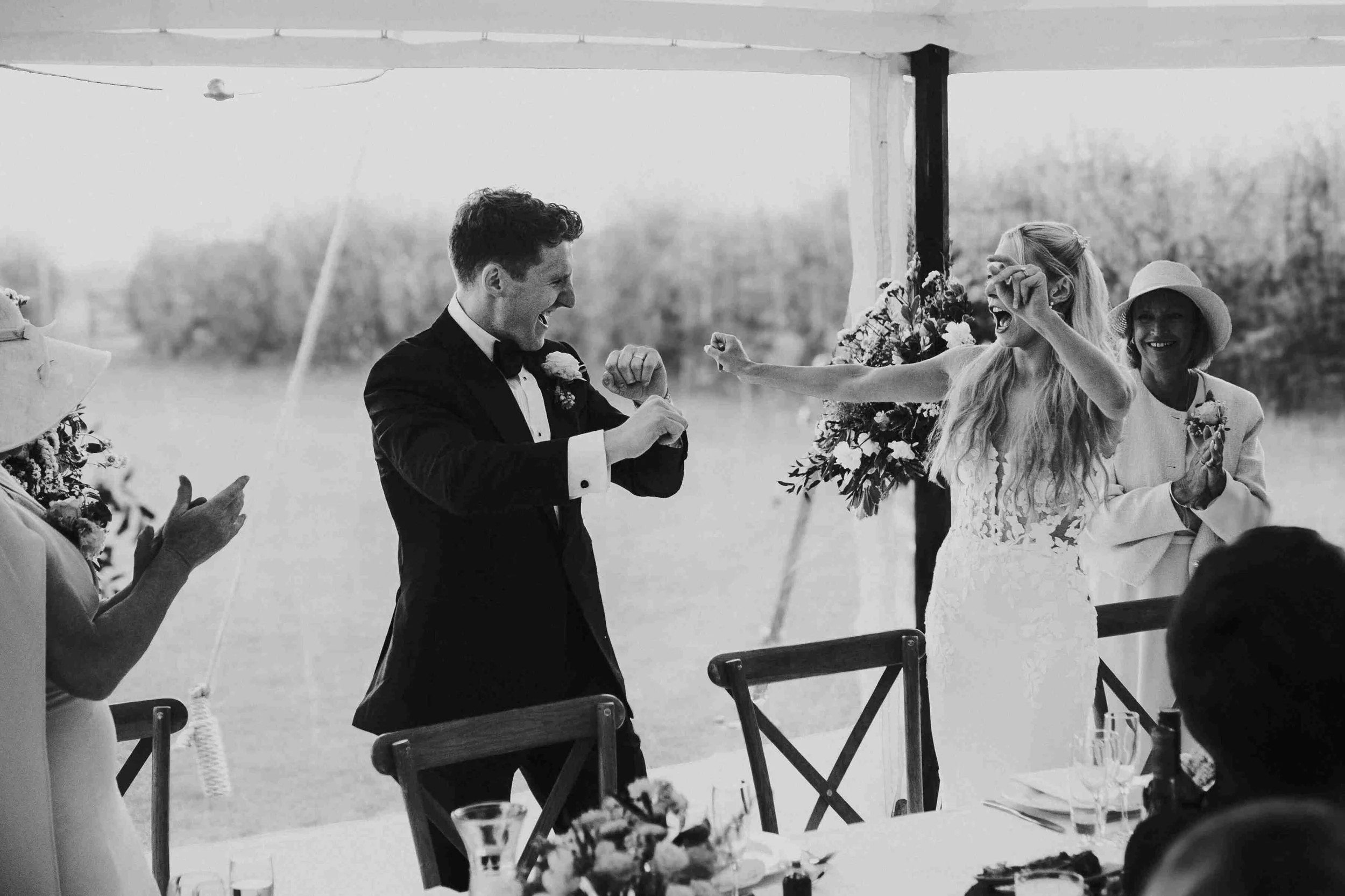 Couple at the top table cheering with guests inside the wedding reception marquee at the Halfmoon Farm Wedding in Rutland
