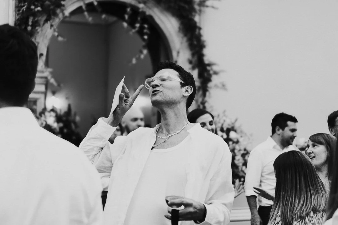 A guest dancing with his eyes closed and throwing a peace sign, whilst wearing heart-shaped sunglasses on the dancefloor at a Hampton Court House Wedding.